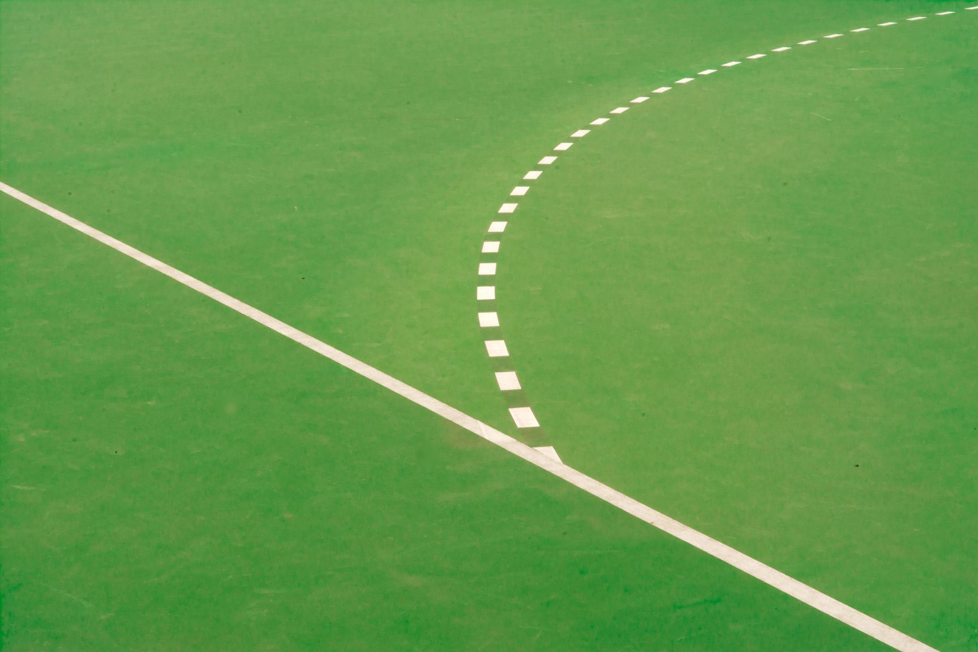Green sports field with a white boundary line and a curved dashed line crossing it