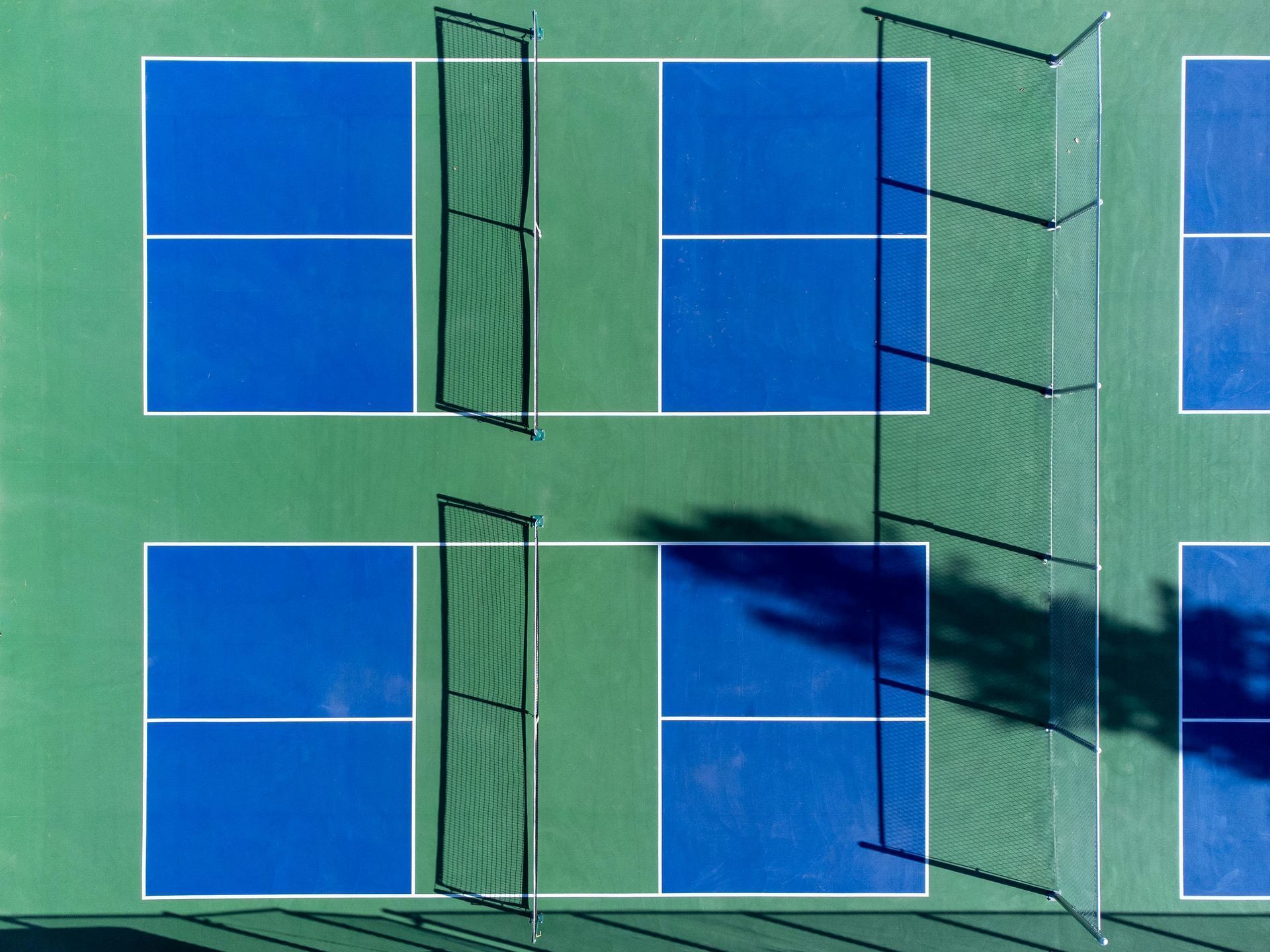 Aerial view of a green tennis court with blue service boxes and court shadows.