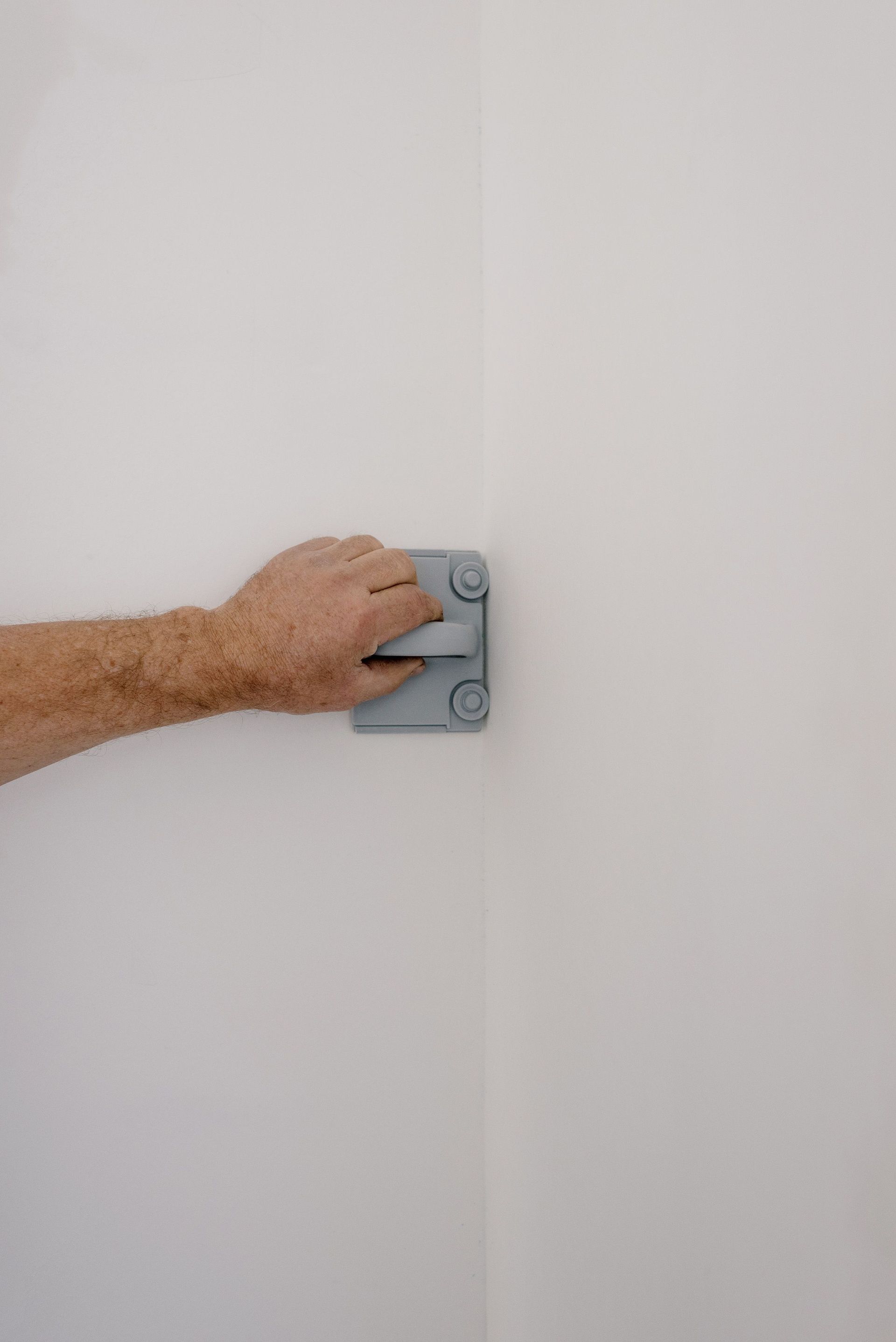 Hand holding a gray wall-mounted bracket against a white wall