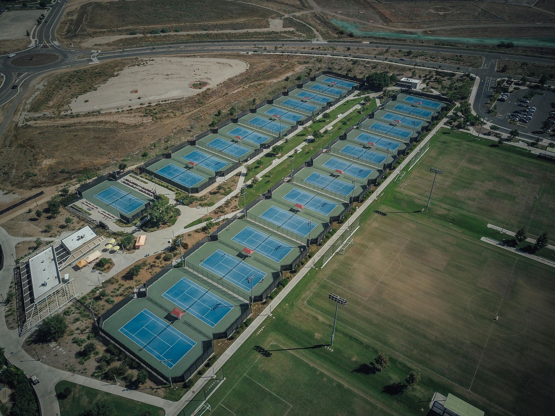 Aerial view of a long row of blue-roofed buildings beside fields and rural roads.