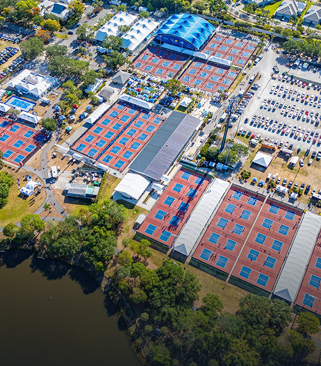 Aerial view of a riverside outdoor sports complex with blue and red courts and parking lots.