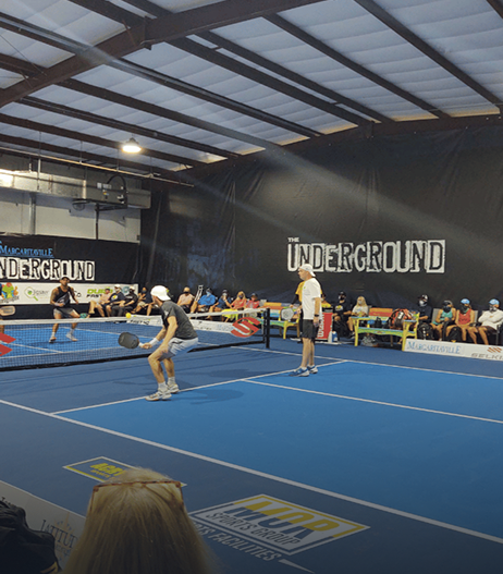 Gymnastics floor practice in a blue indoor gym with athletes and spectators under “UNDERGROUND” banners