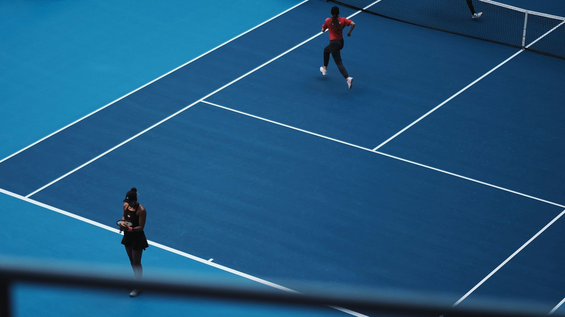 Two tennis players on a blue court during a match, one near the baseline and one at the net