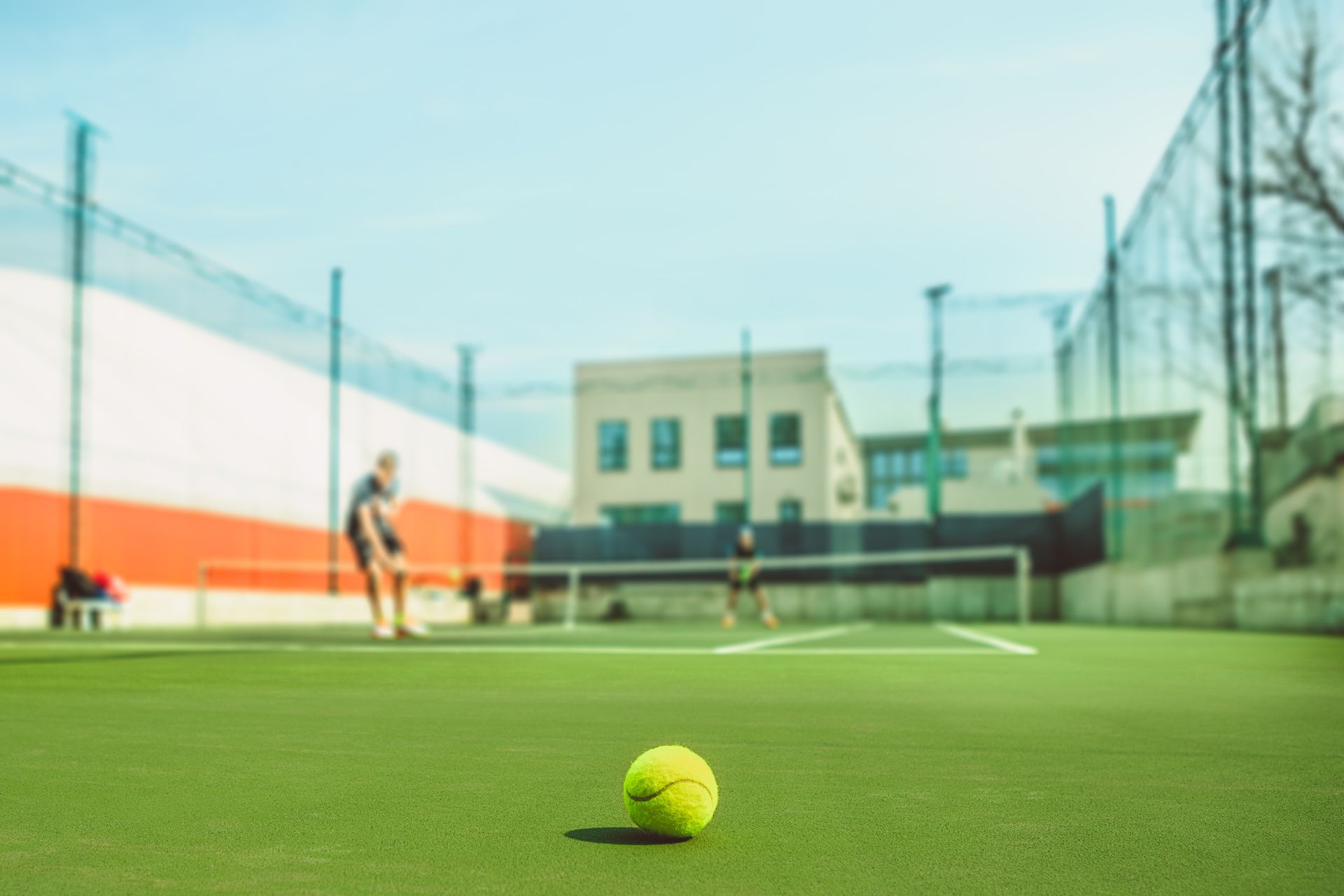 Tennis ball on green court with a player in the background near the net