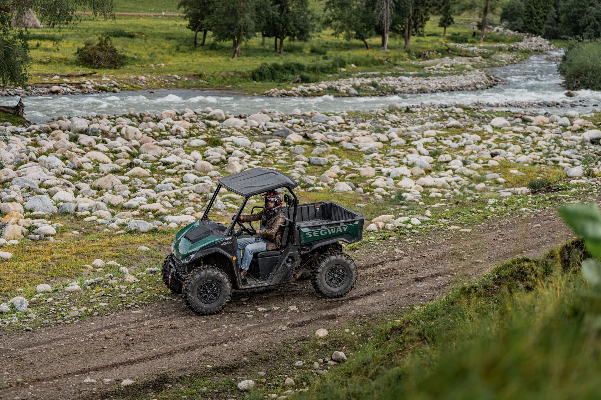 A Person Drives a Green Utv on A Dirt Path Alongside a Rocky River — Whitsunday Mowers In Airlie Beach, QLD
