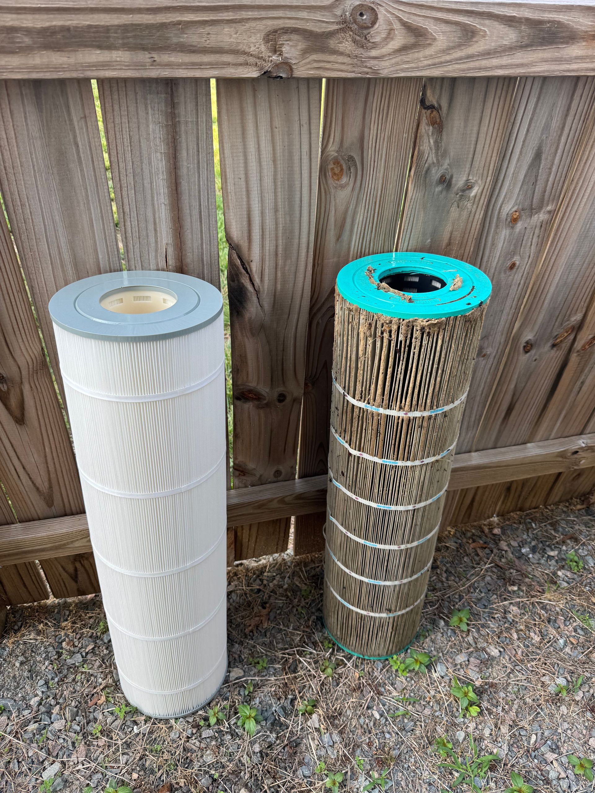 Two rolled materials, one white and one tan, standing against a wooden fence outdoors.
