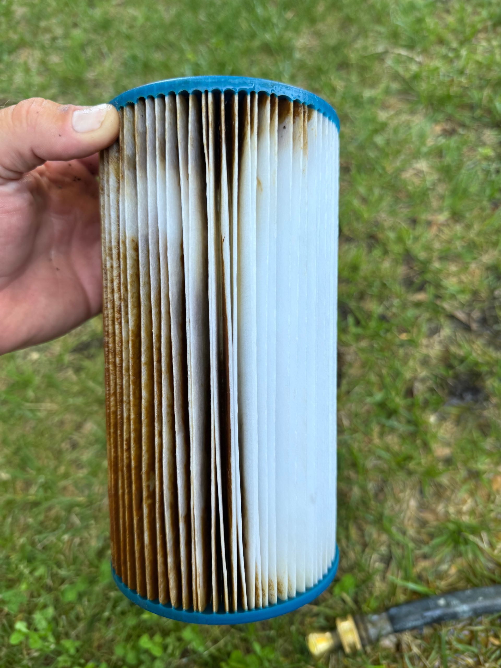 Dirty pleated air filter held outdoors by a hand, with brown and white vertical pleats.
