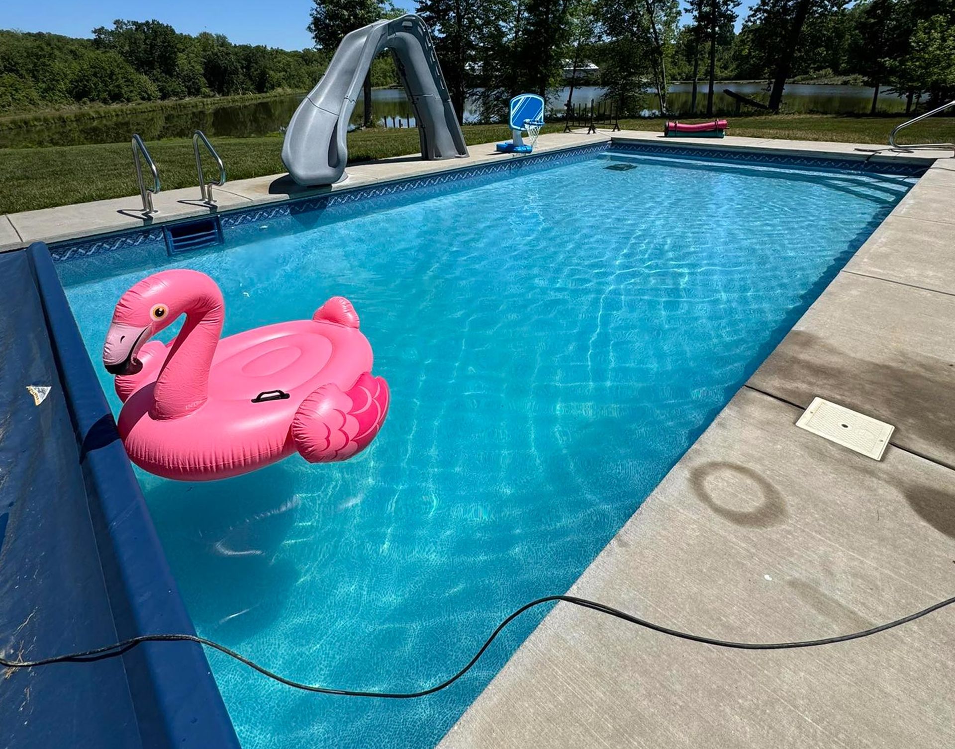 Pink flamingo pool float in a sunny backyard swimming pool with a slide and concrete deck