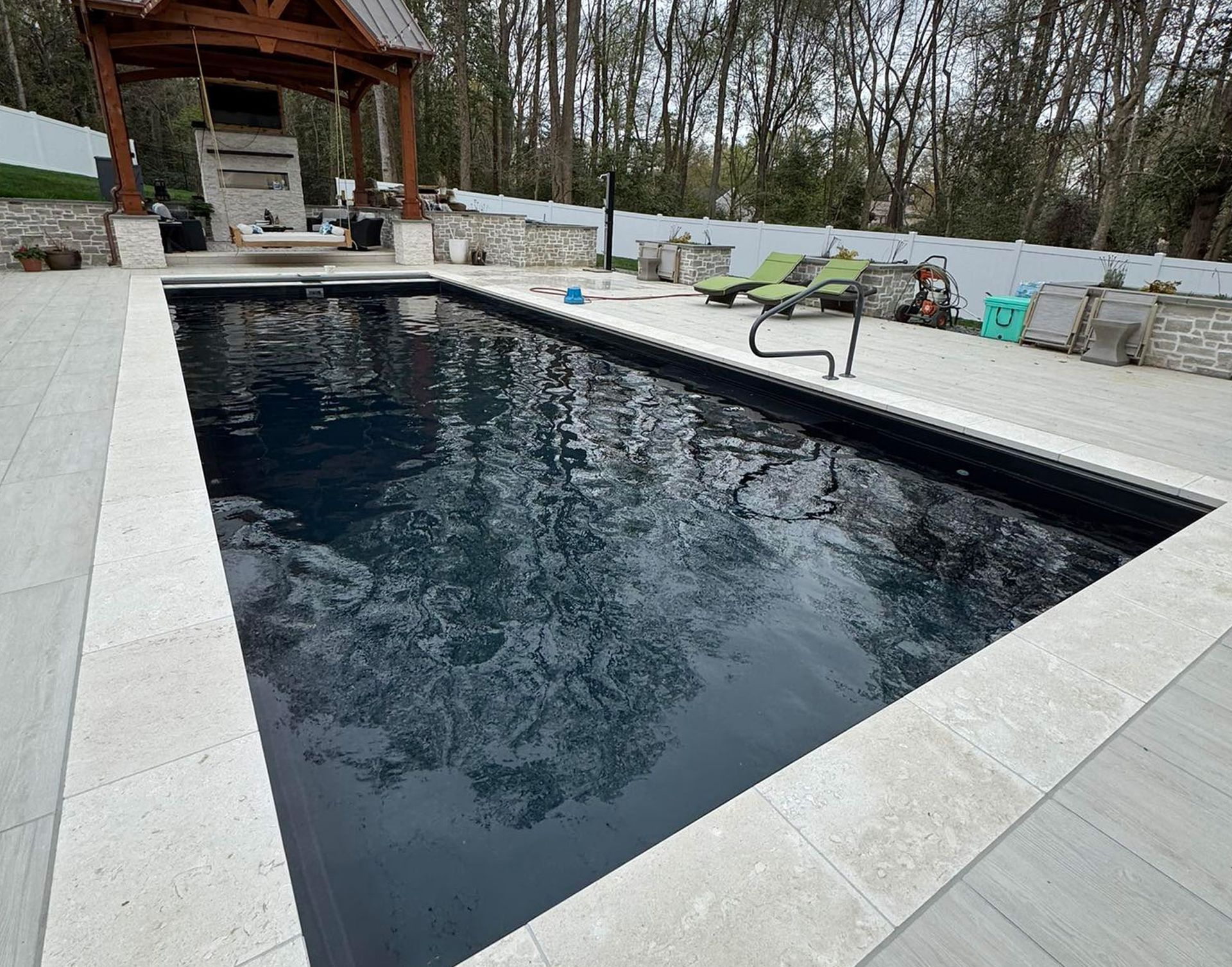 Rectangular backyard pool with dark water, white stone deck, and a covered patio in the background