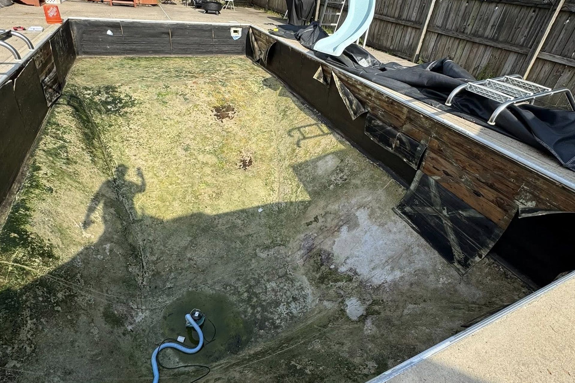 Empty backyard pool with dirty green water, debris, and a blue hose on the floor