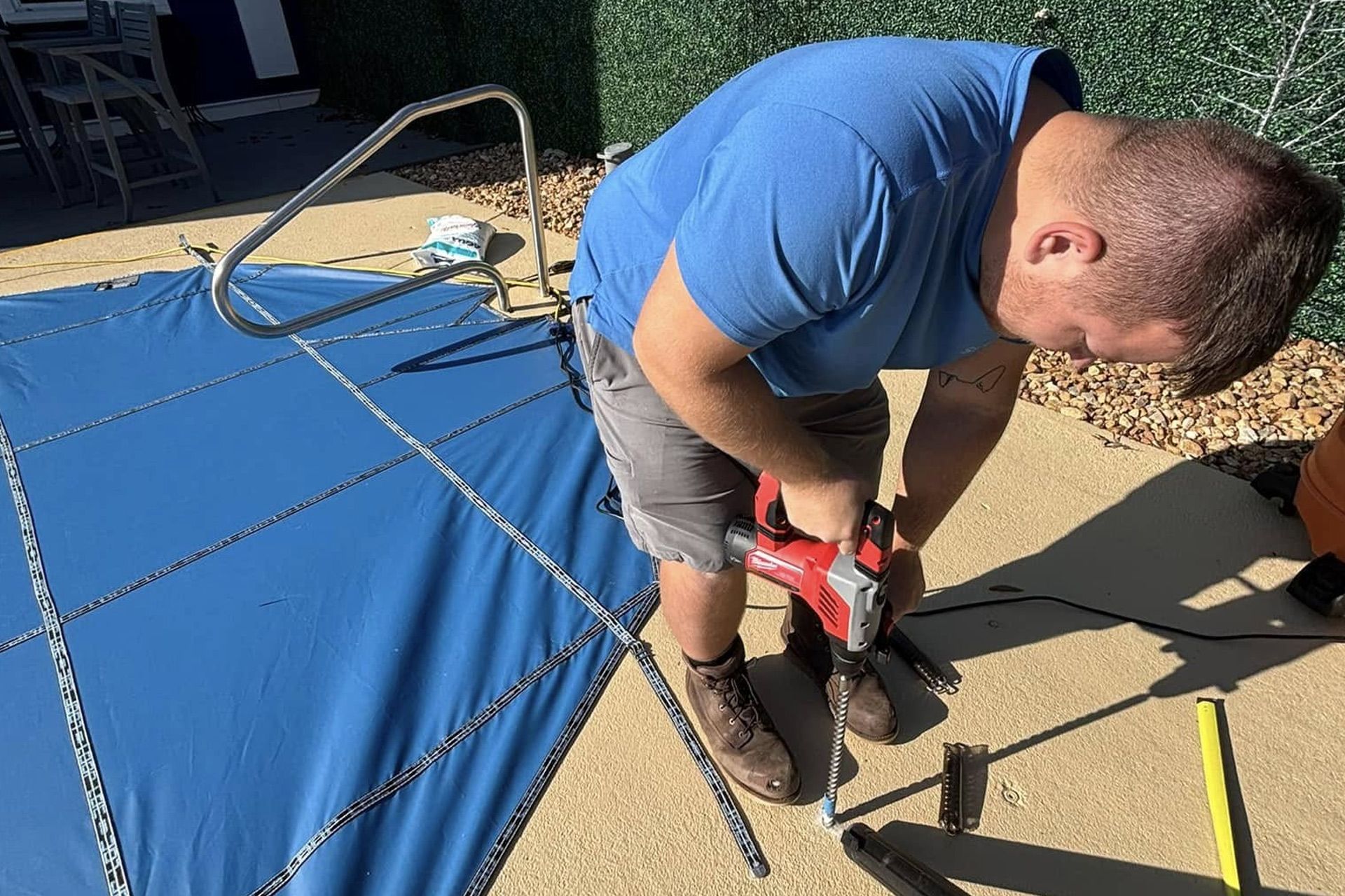 Person using a red power drill on a blue patio cover frame outdoors