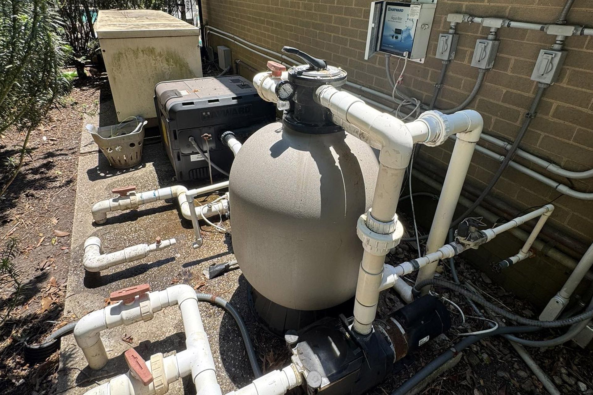 Outdoor pool pump and filtration equipment with white pipes beside a house wall