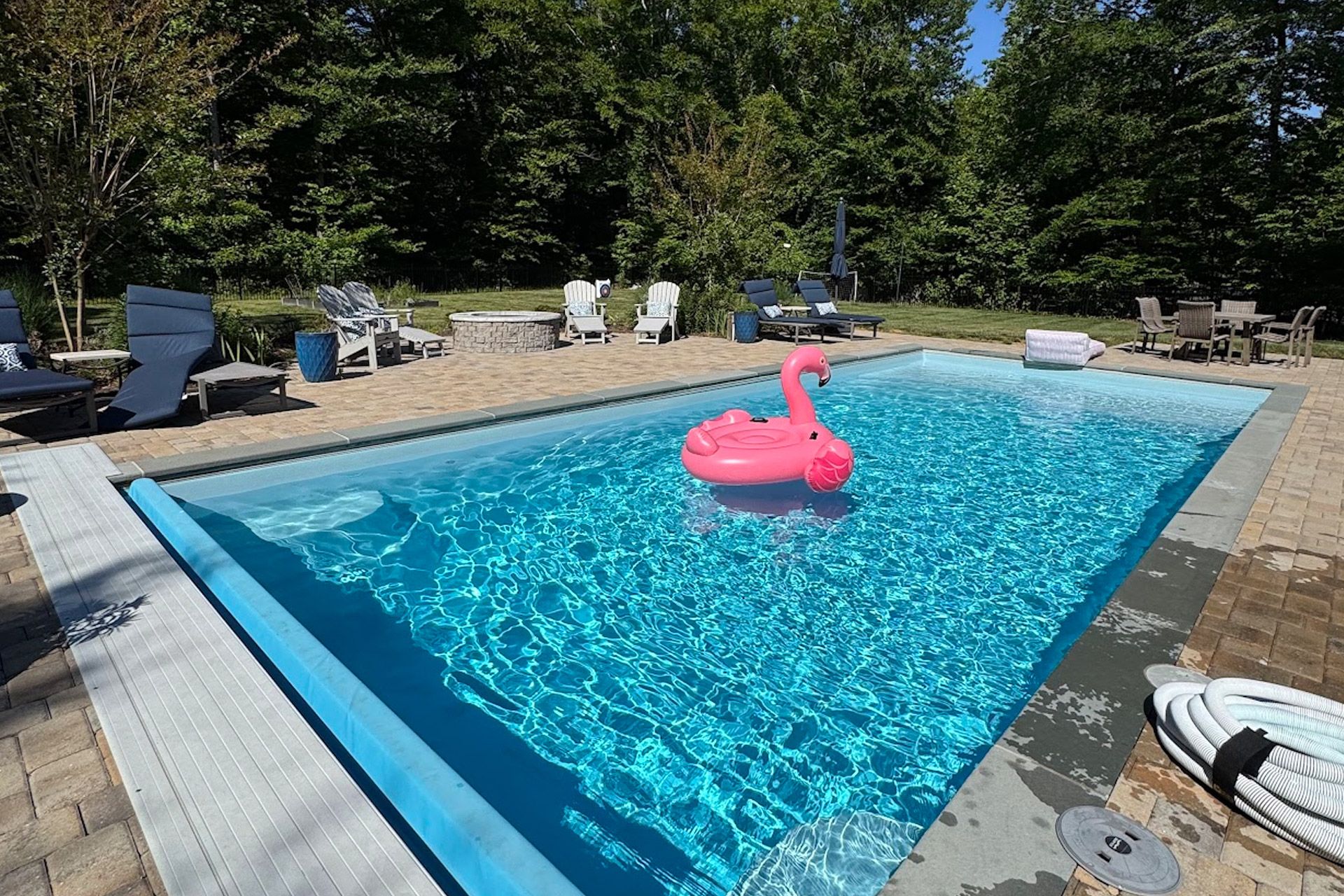 Backyard swimming pool with a pink flamingo float, lounge chairs, and trees in the background