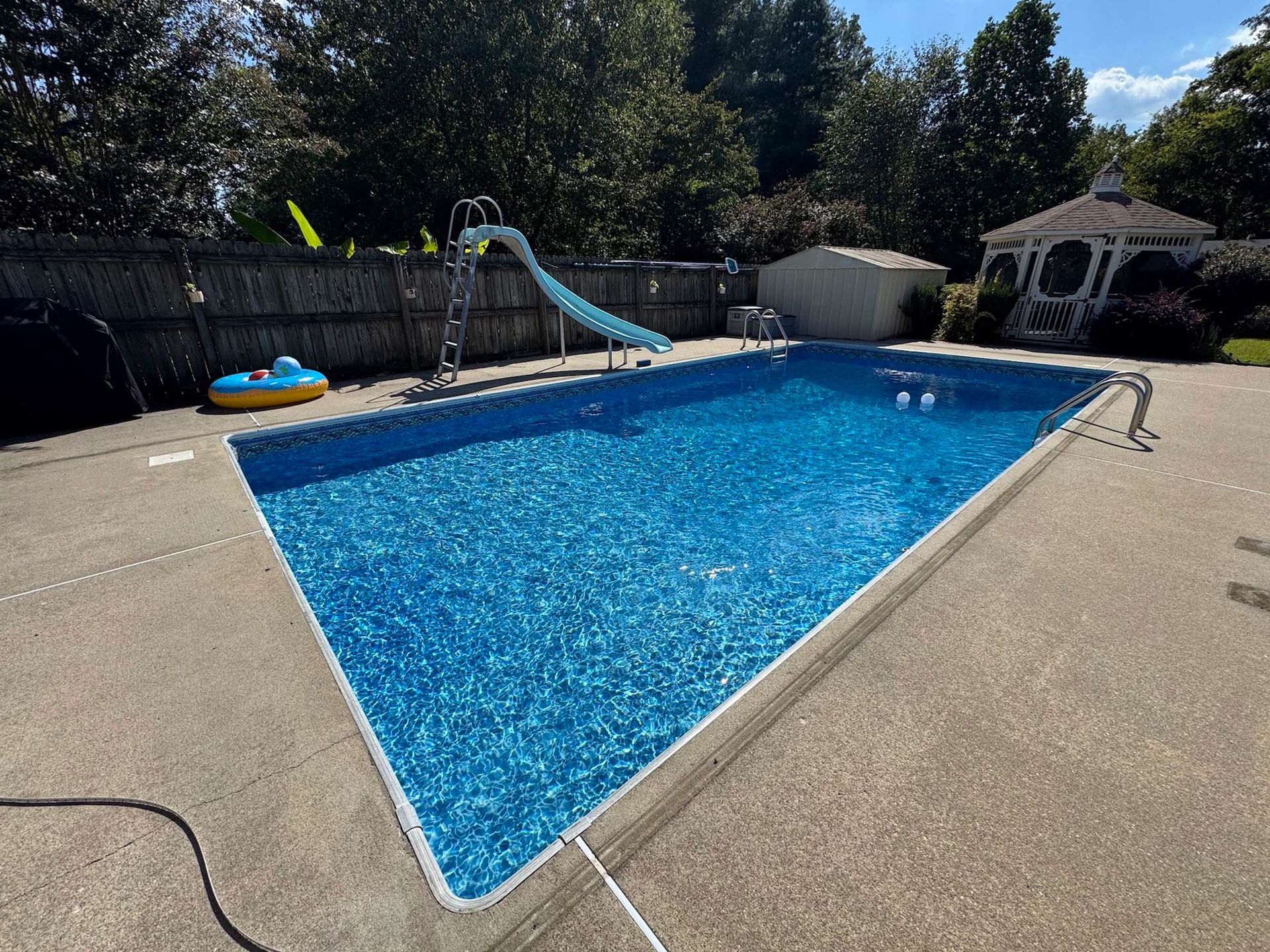 Backyard swimming pool with a slide, concrete deck, and gazebo on a sunny day