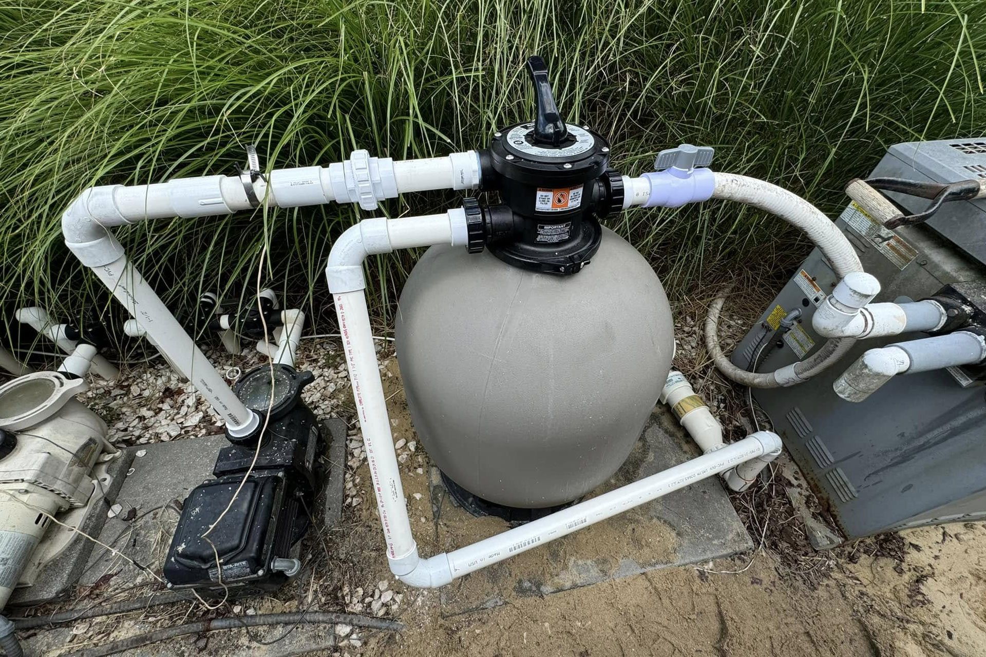 Pool filter system with a round tank, pipes, and pump equipment beside a grassy area