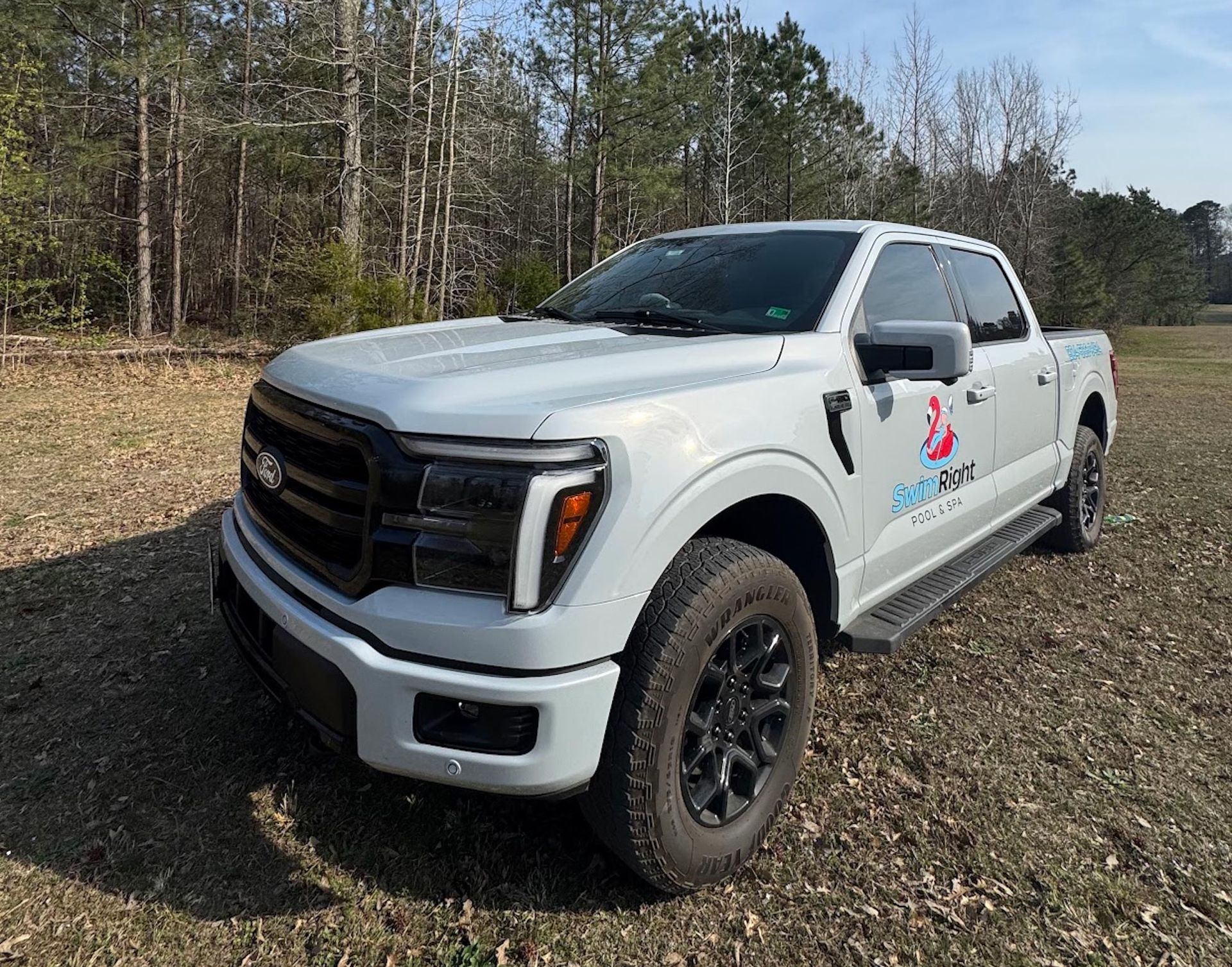 White pickup truck parked on a dirt path beside a wooded area on a sunny day