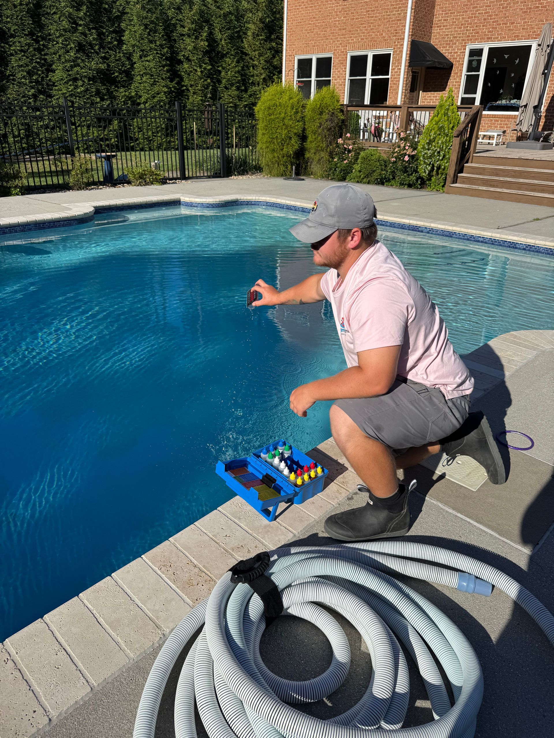 Man kneels beside a pool, reaching toward the water with a tray of items nearby.