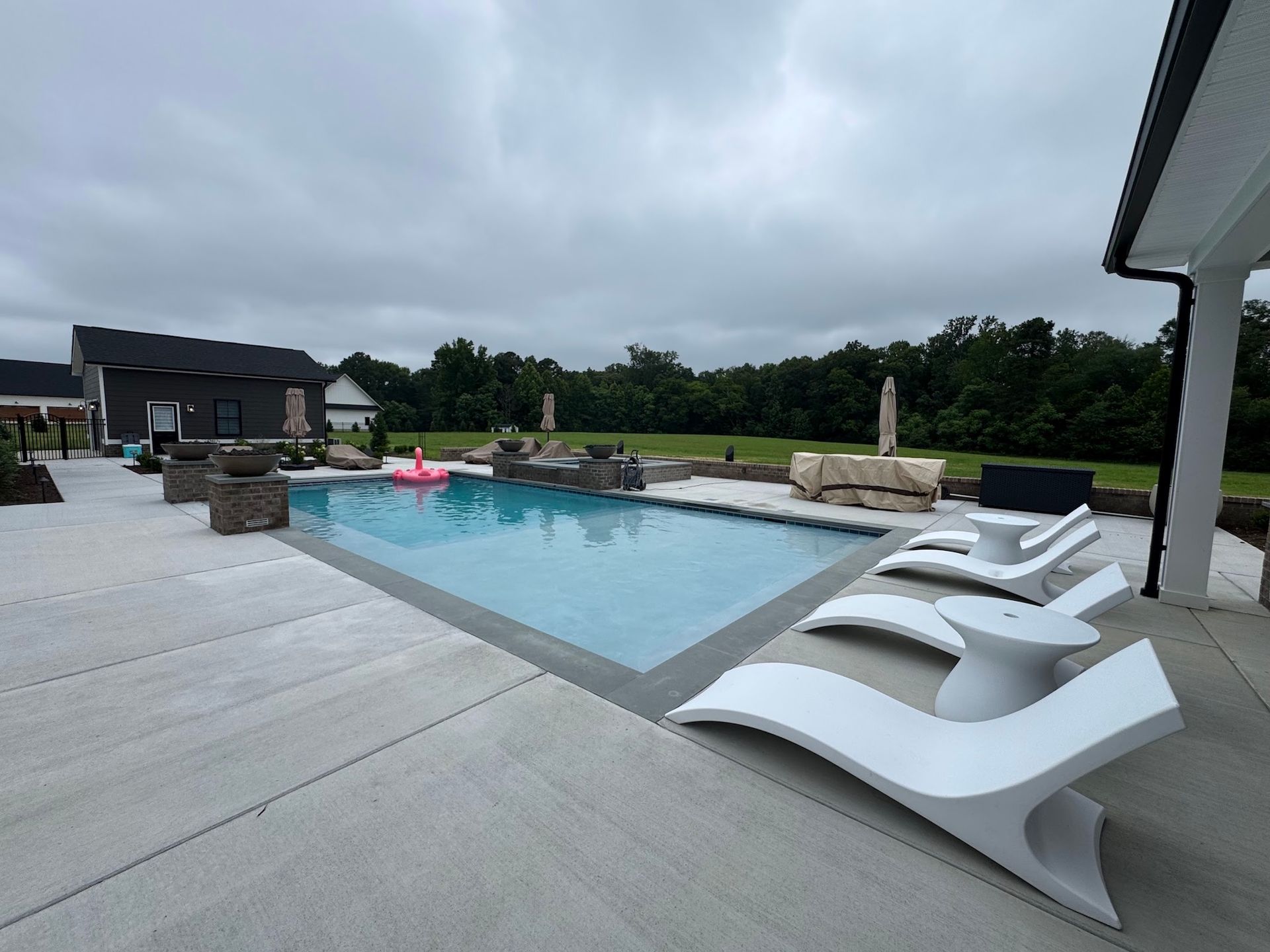 Modern backyard pool with lounge chairs, cloudy sky, and patio deck