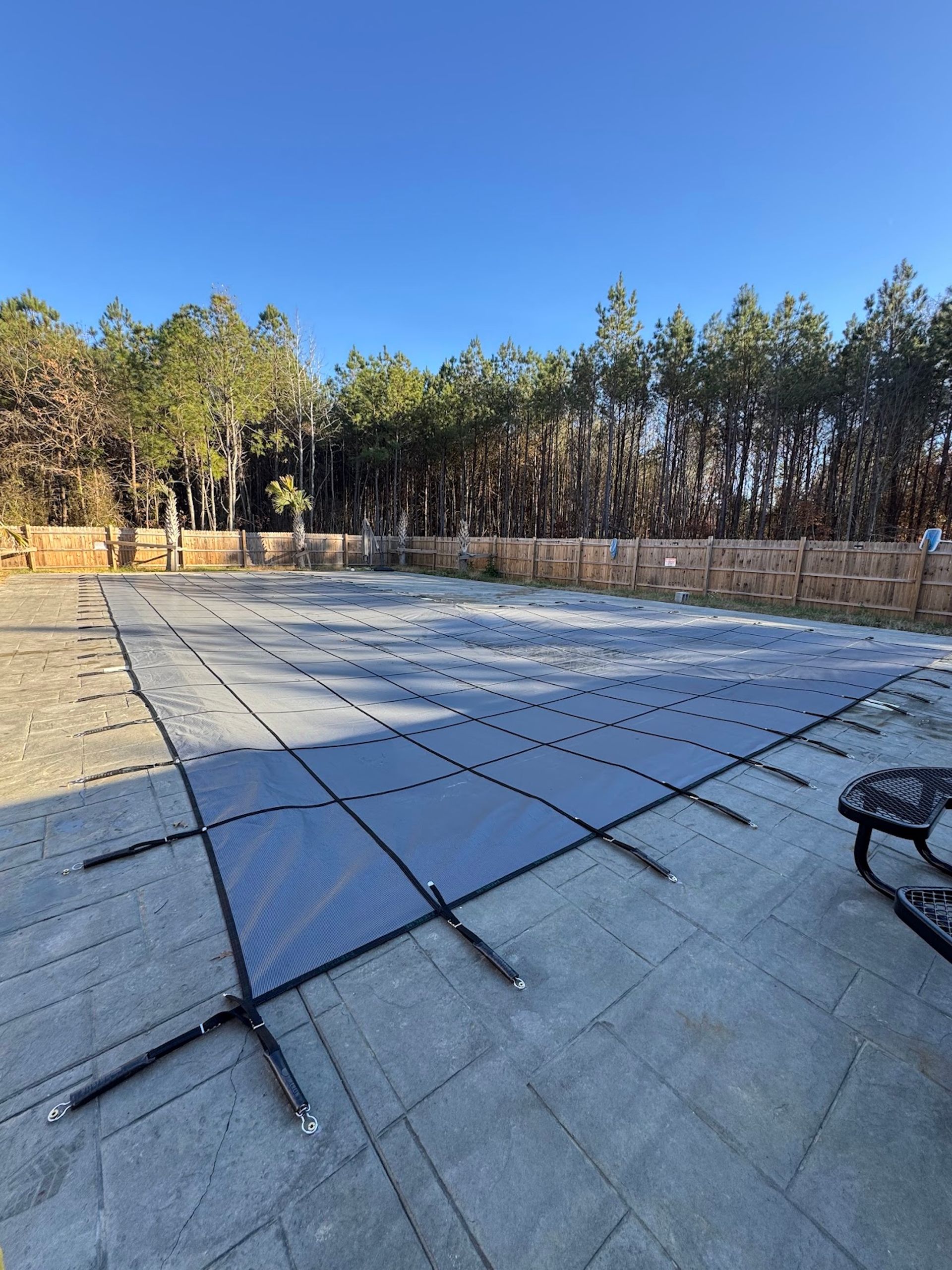 Outdoor concrete patio with a stone retaining wall, trees, and clear blue sky.