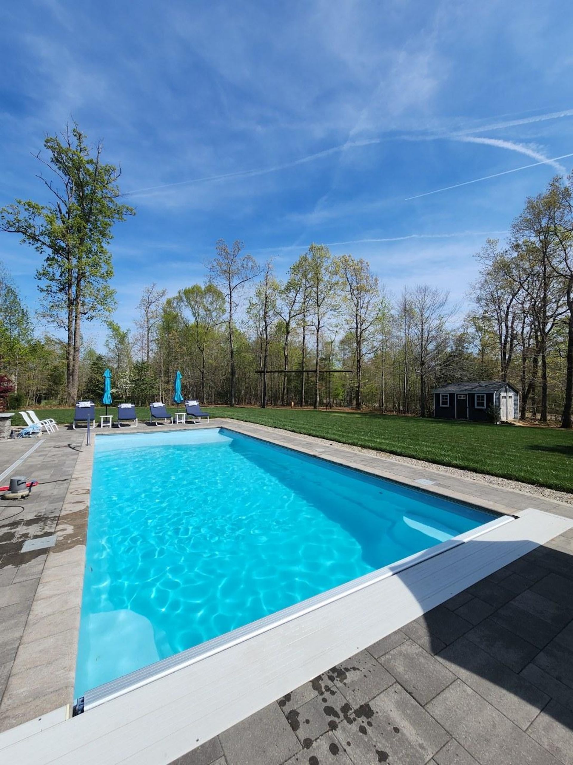 Outdoor swimming pool with bright blue water, white edges, and lounge chairs under a sunny sky.