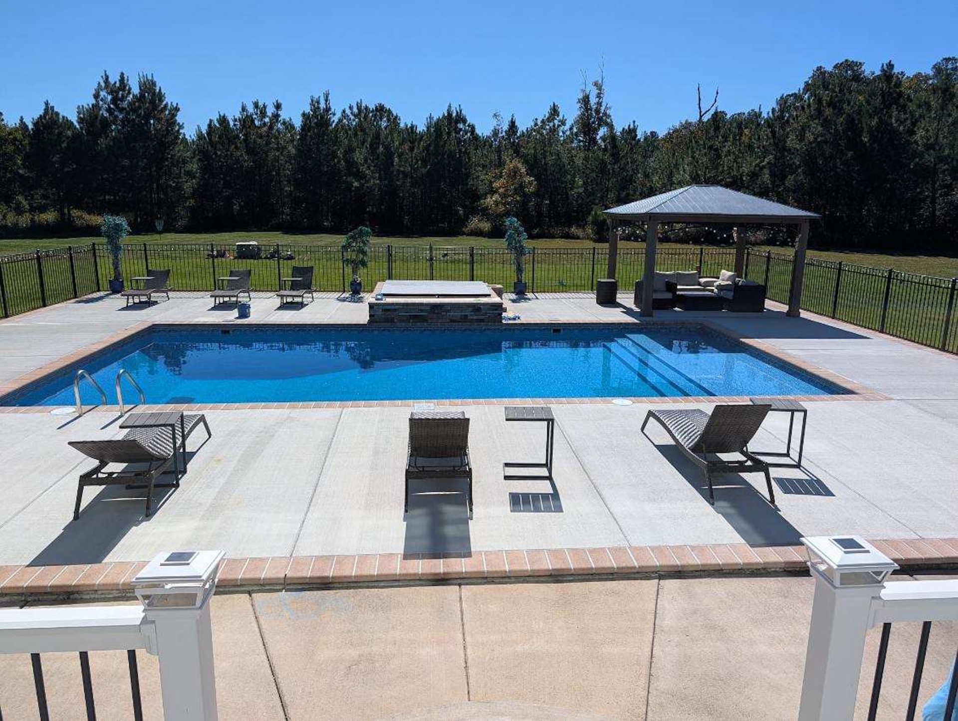Backyard pool with lounge chairs, patio seating, and a covered cabana on a sunny day