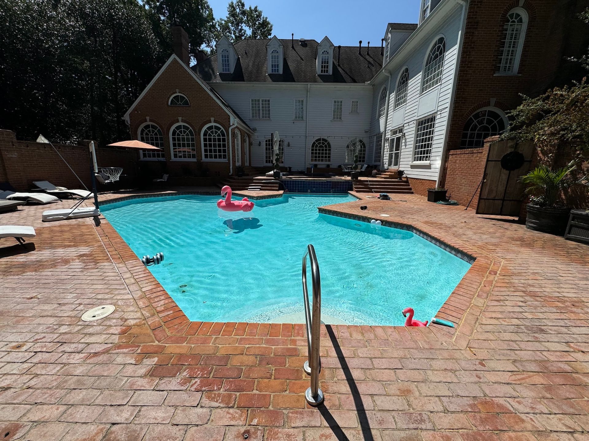 Courtyard swimming pool with blue water, brick patio, lounge chairs, and white buildings surrounding it