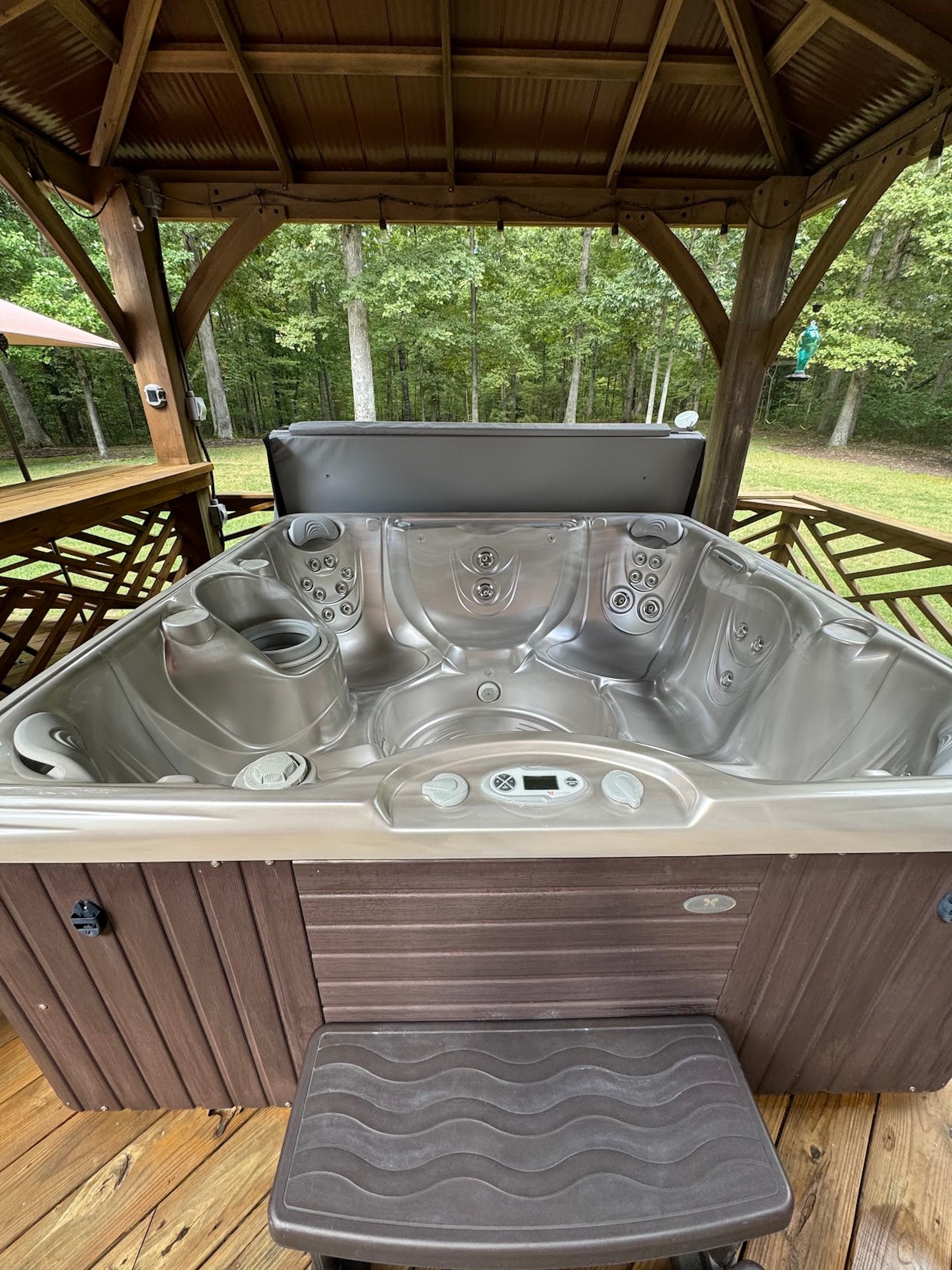 Stainless steel hot tub under a wooden gazebo, with forest greenery in the background.