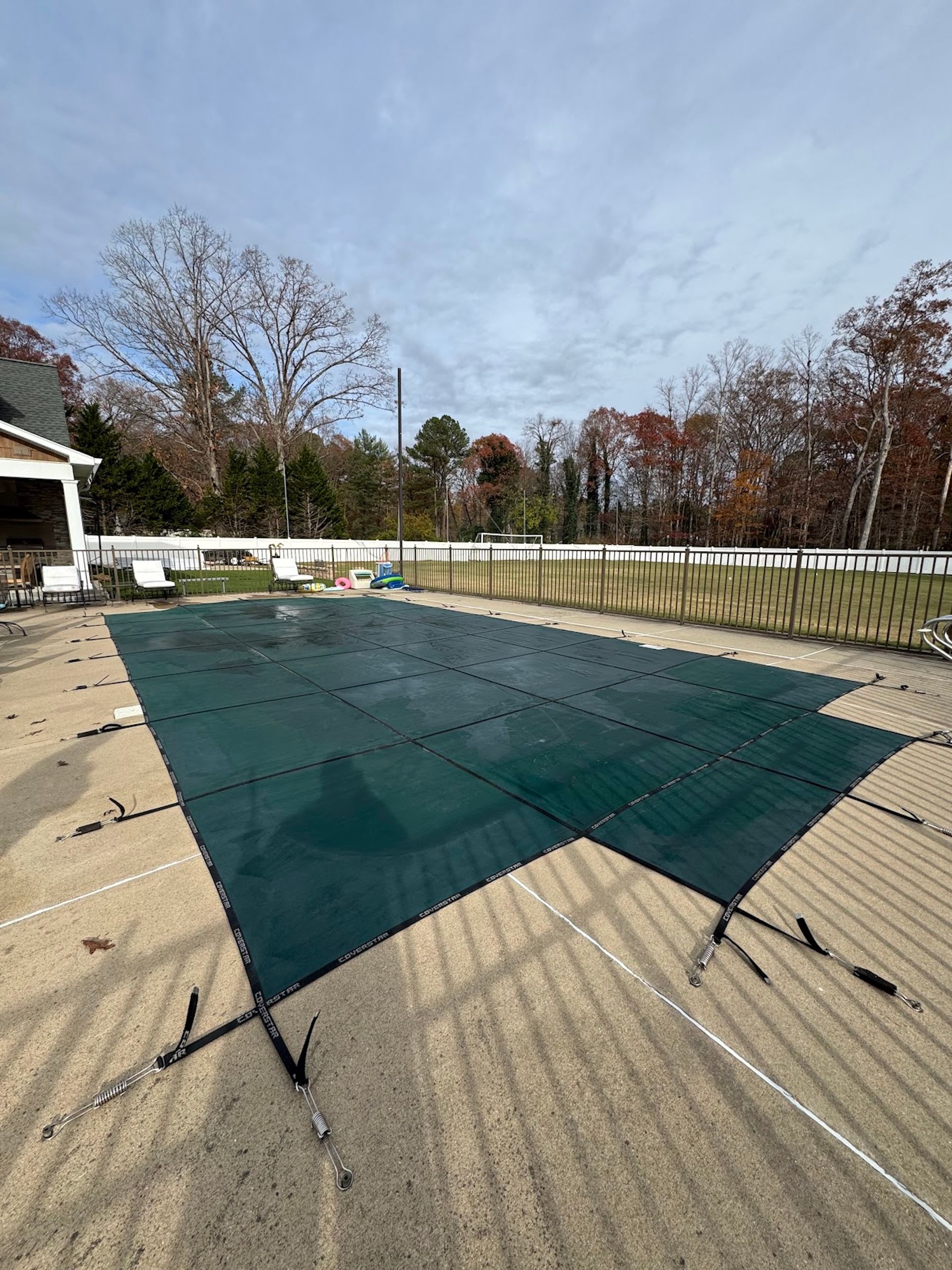 Green shade sail stretched over a patio beside a house, with trees and a fence in the background