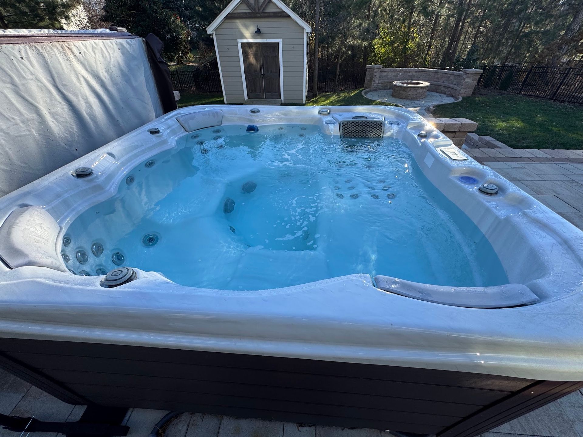 Snow-covered backyard hot tub with blue water and a small shed in the background