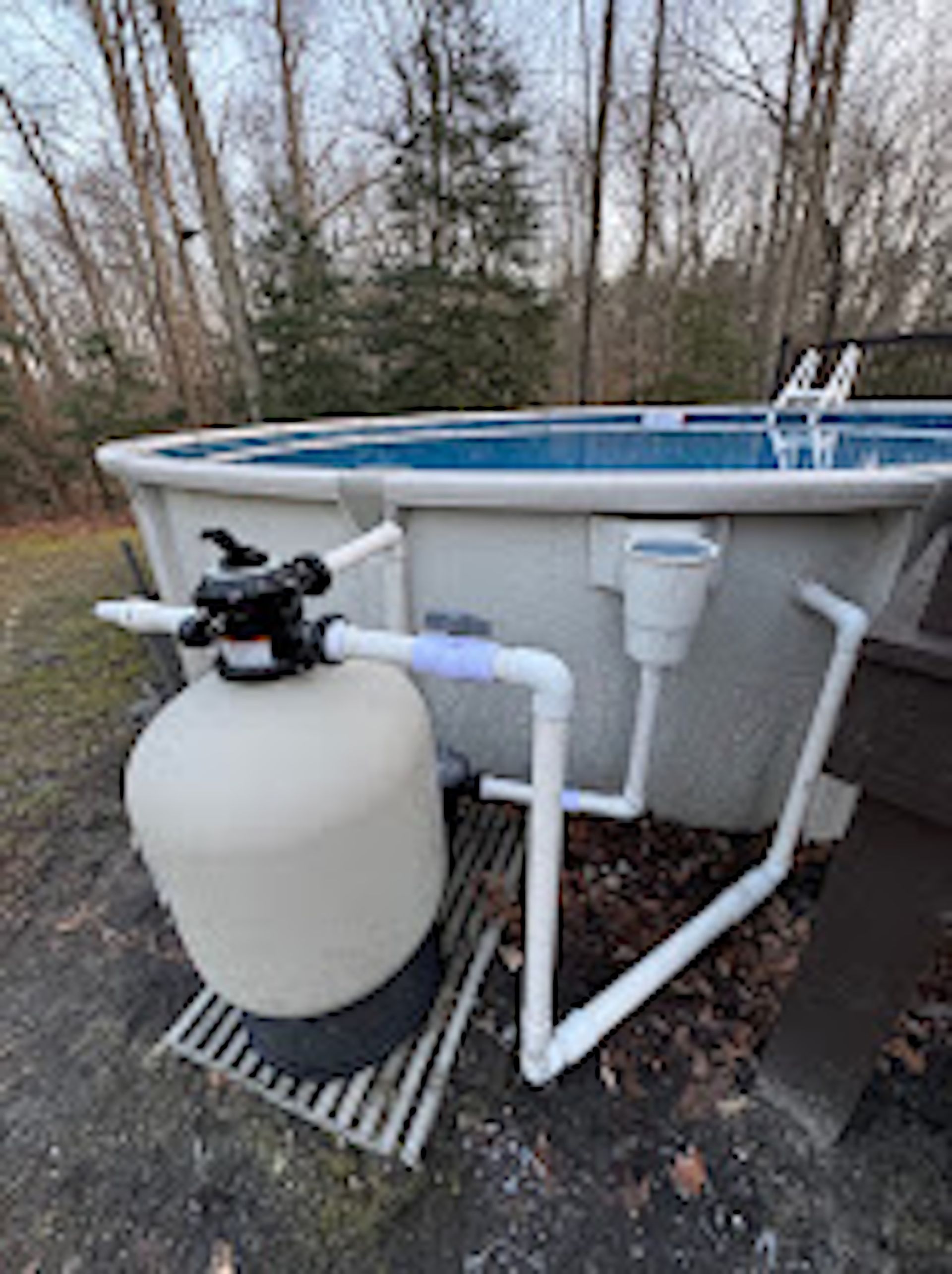 Outdoor above-ground pool with sand filter and white plumbing pipes on a wet driveway