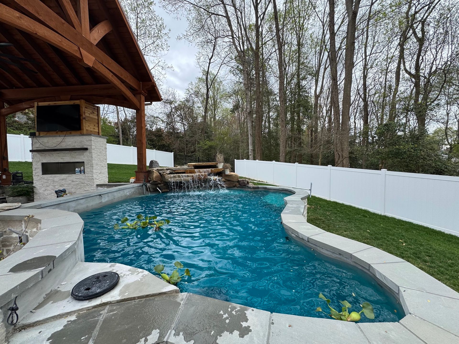 Backyard pool with a curved blue water feature, white patio, and covered outdoor fireplace area