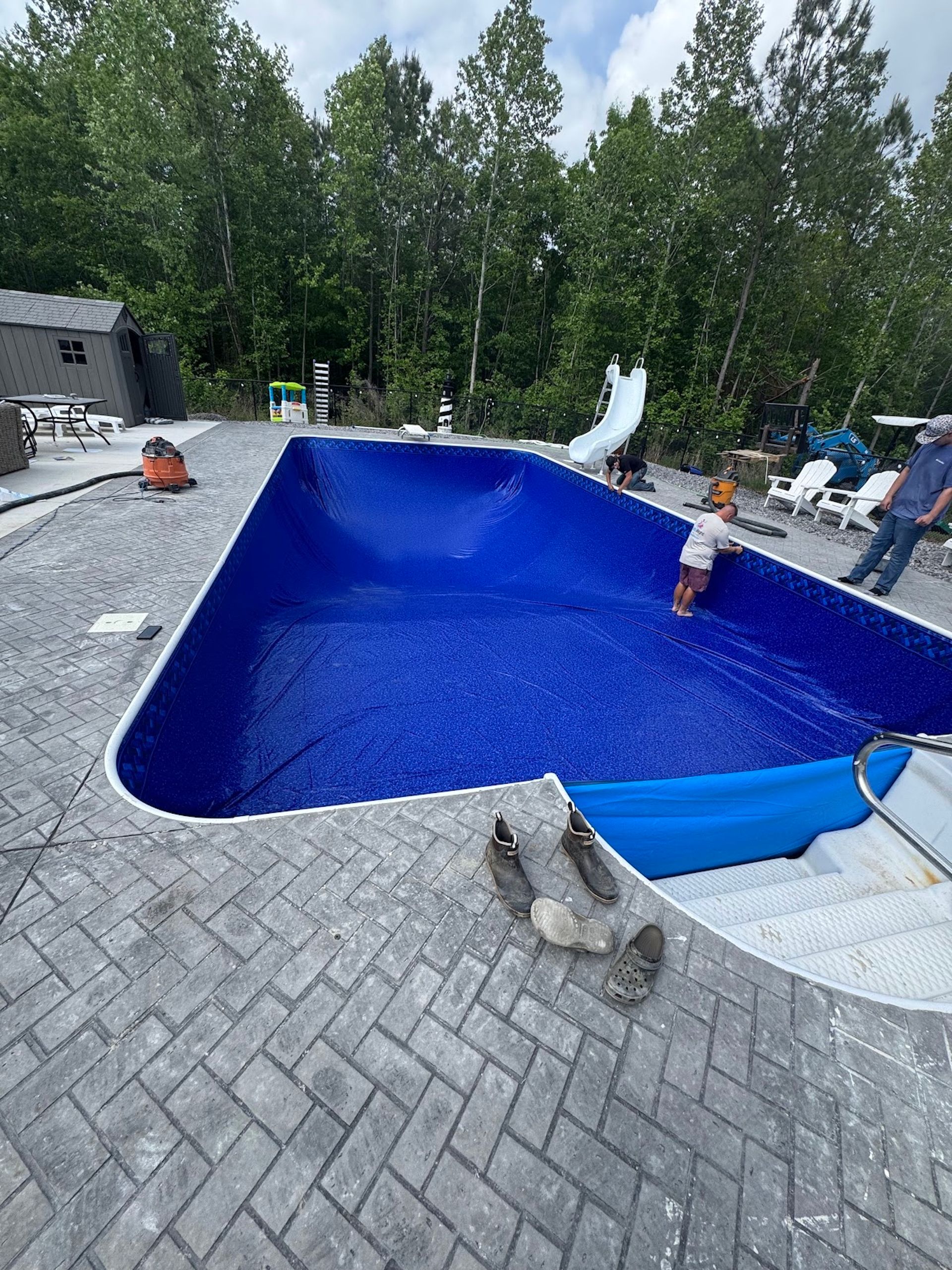 Backyard pool being lined with bright blue material, with people working around the deck.