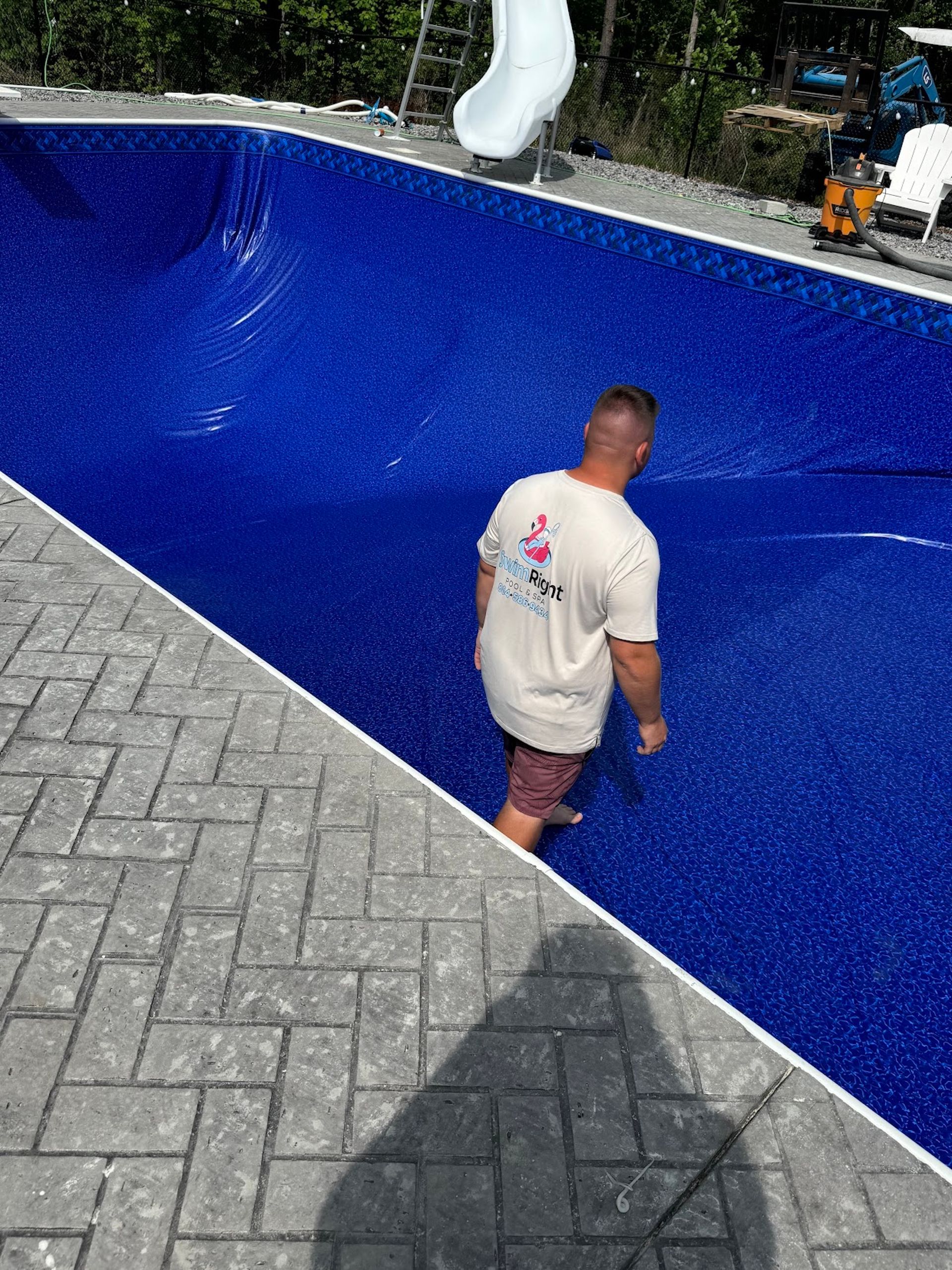 Person standing in an empty blue swimming pool beside gray pavers.