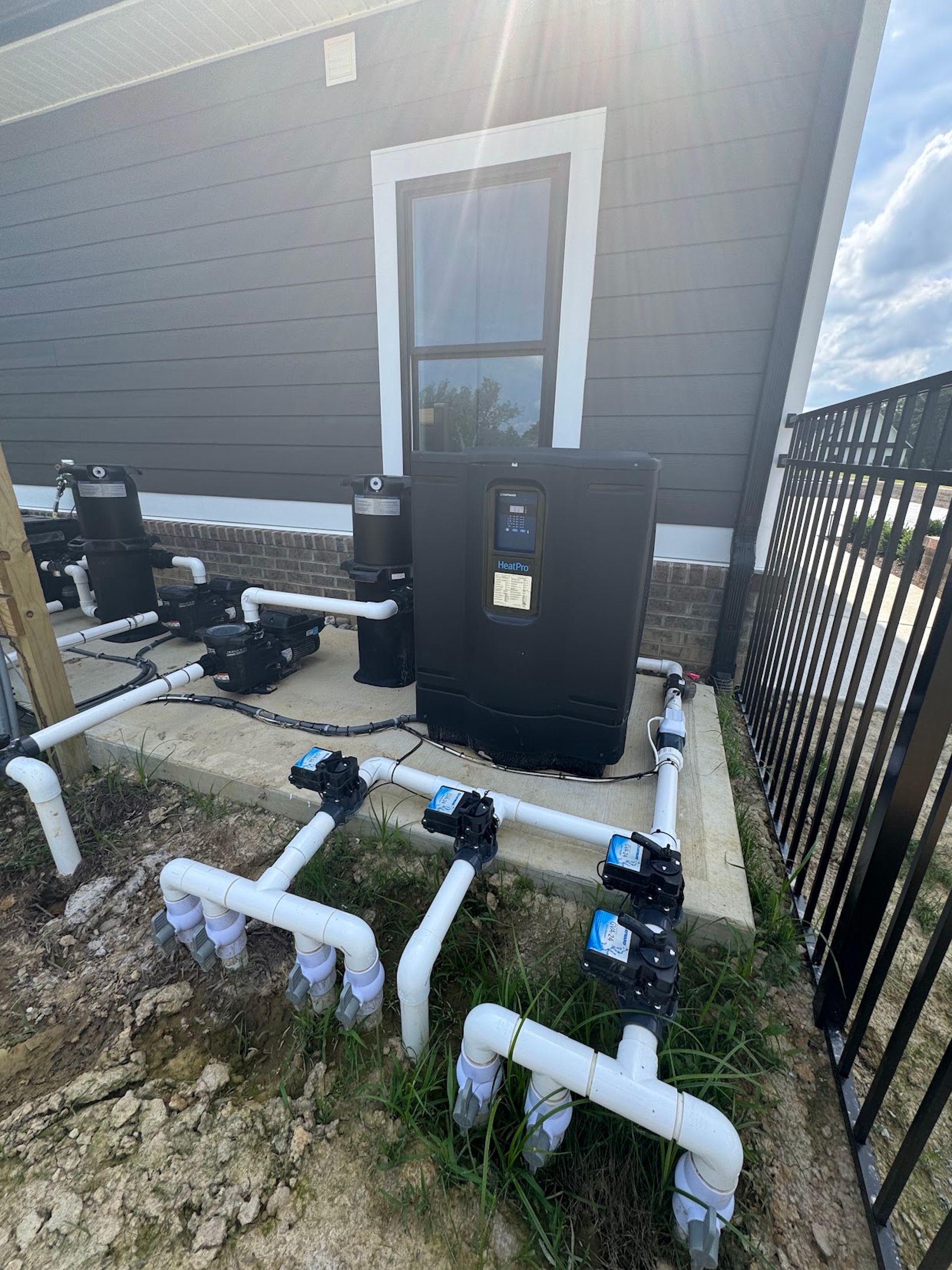 Pool equipment with white PVC pipes beside a house and black utility box on a concrete pad