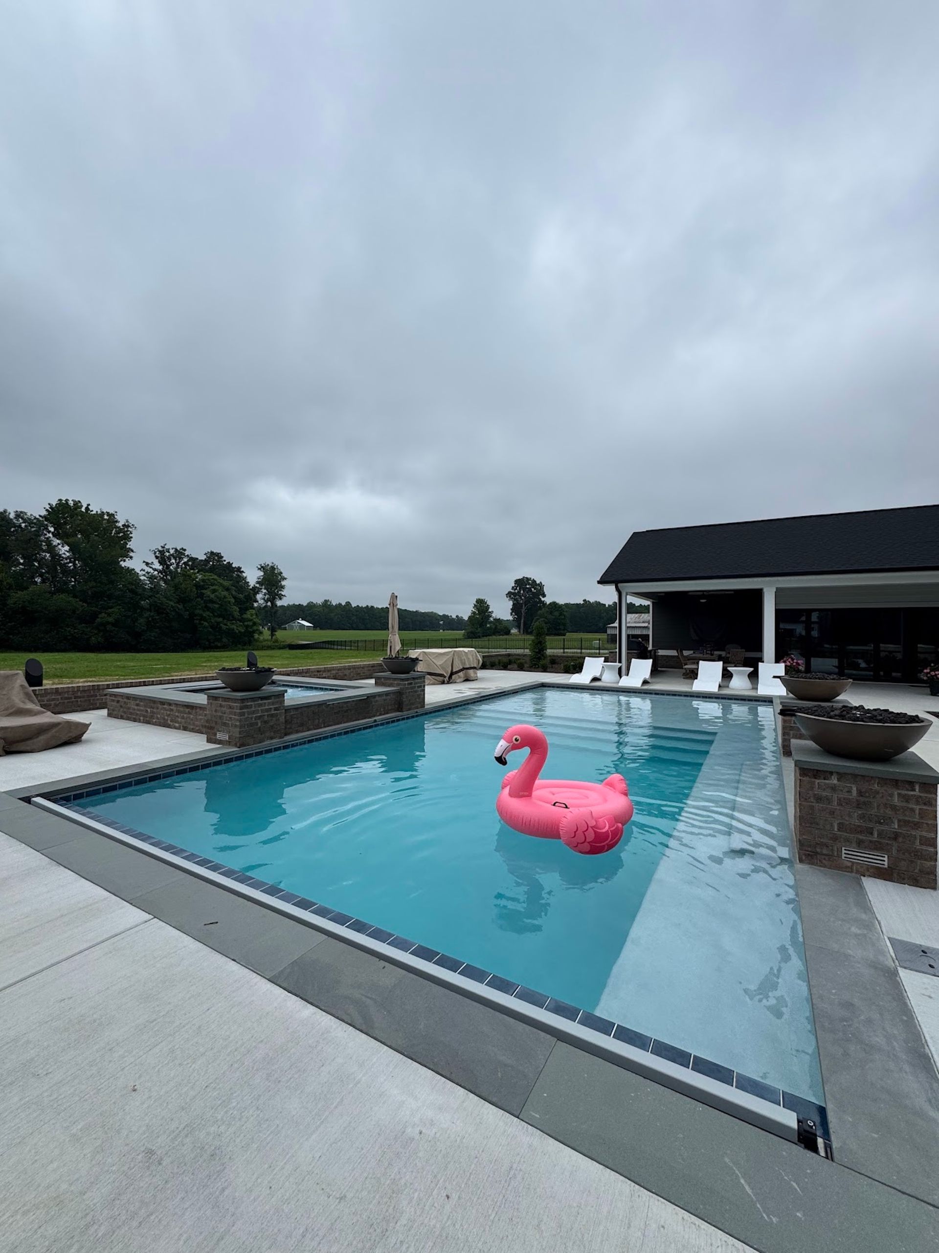 Modern backyard pool with a pink flamingo float under a cloudy sky