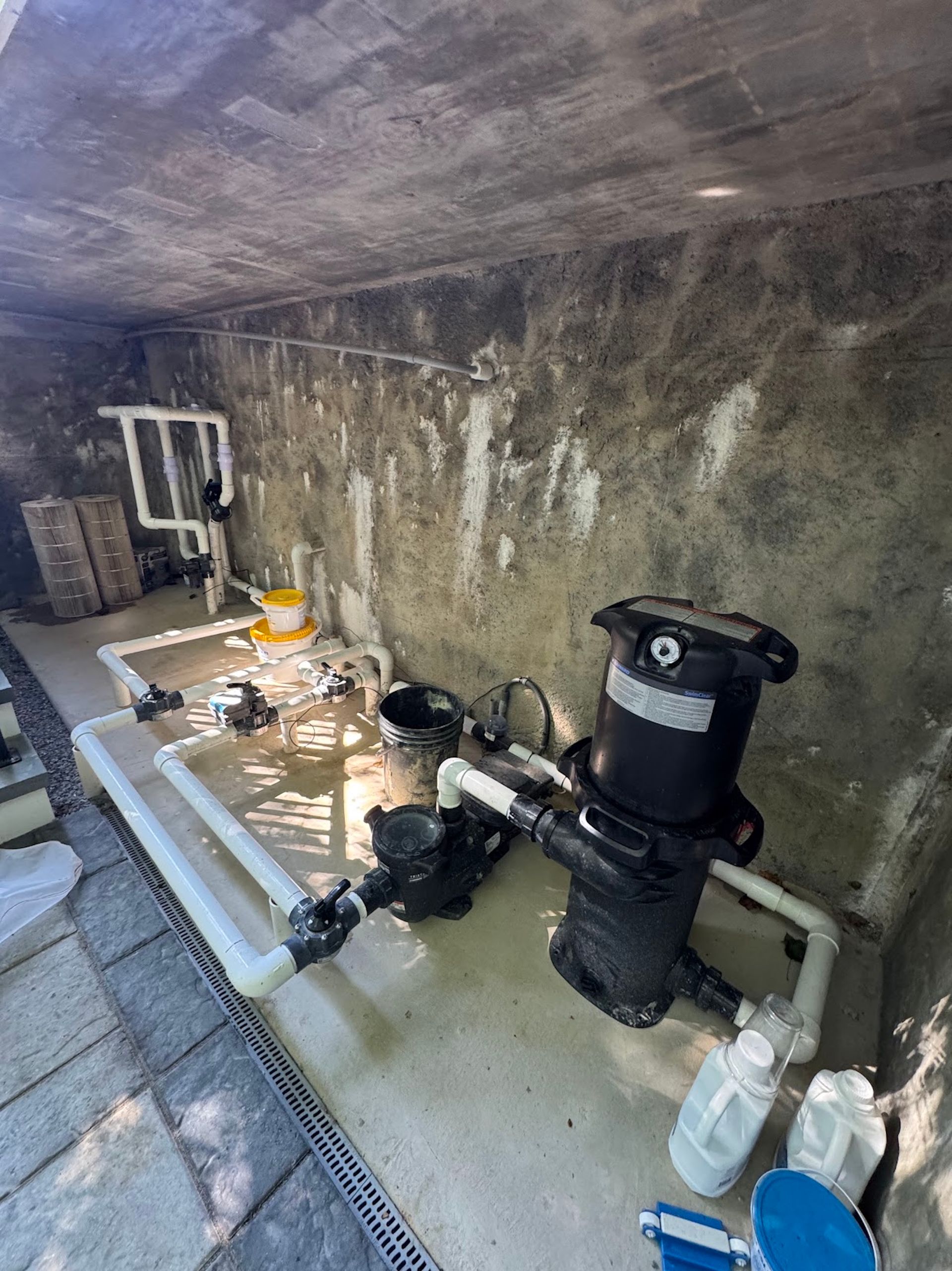 Damp basement utility room with pipes, pump, and water on the floor against a stained concrete wall