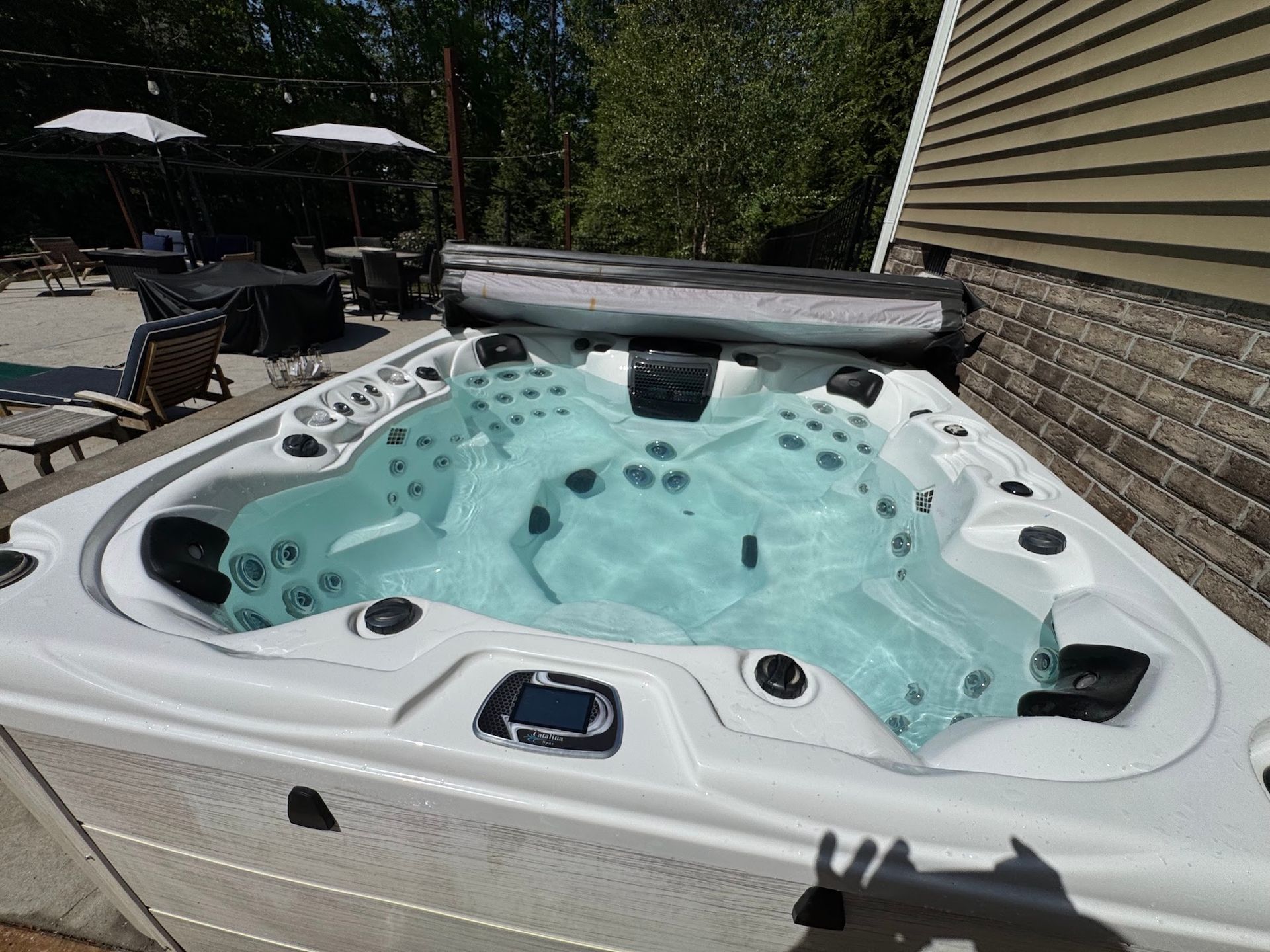 White hot tub filled with turquoise water on a sunny patio near outdoor lounge chairs