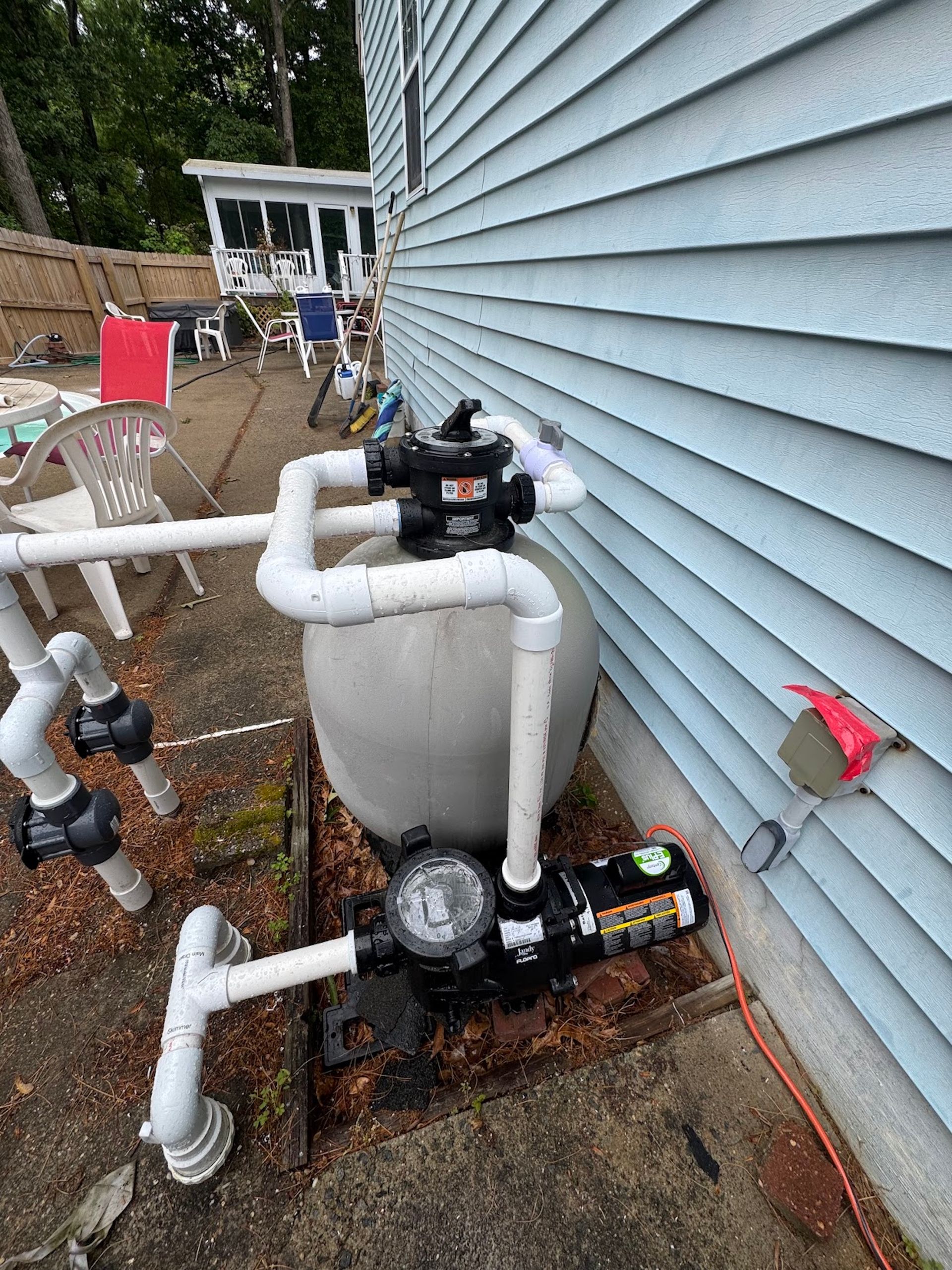 Pool pump and PVC piping mounted beside a house with blue siding.