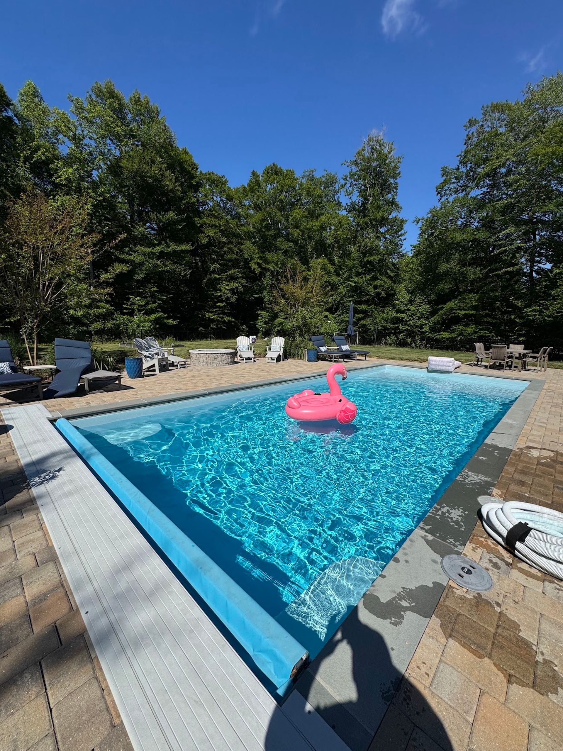 Backyard pool with blue water, lounge chairs, and a pink flamingo float under a clear sky