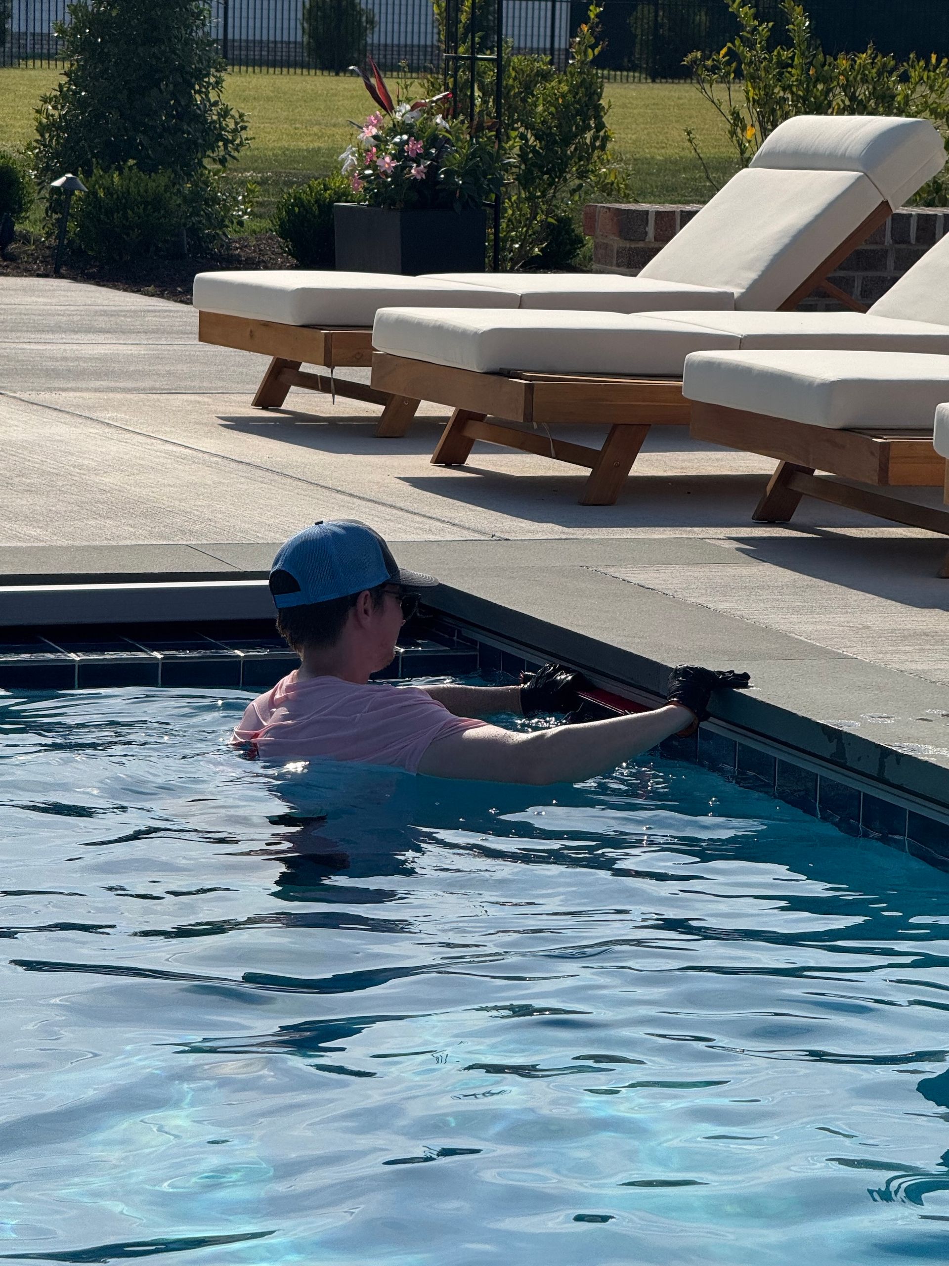 Person in a blue cap floating in a pool near lounge chairs on a sunny deck