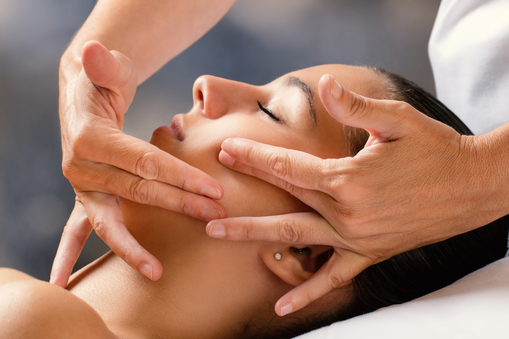 A woman is getting a facial massage with her eyes closed