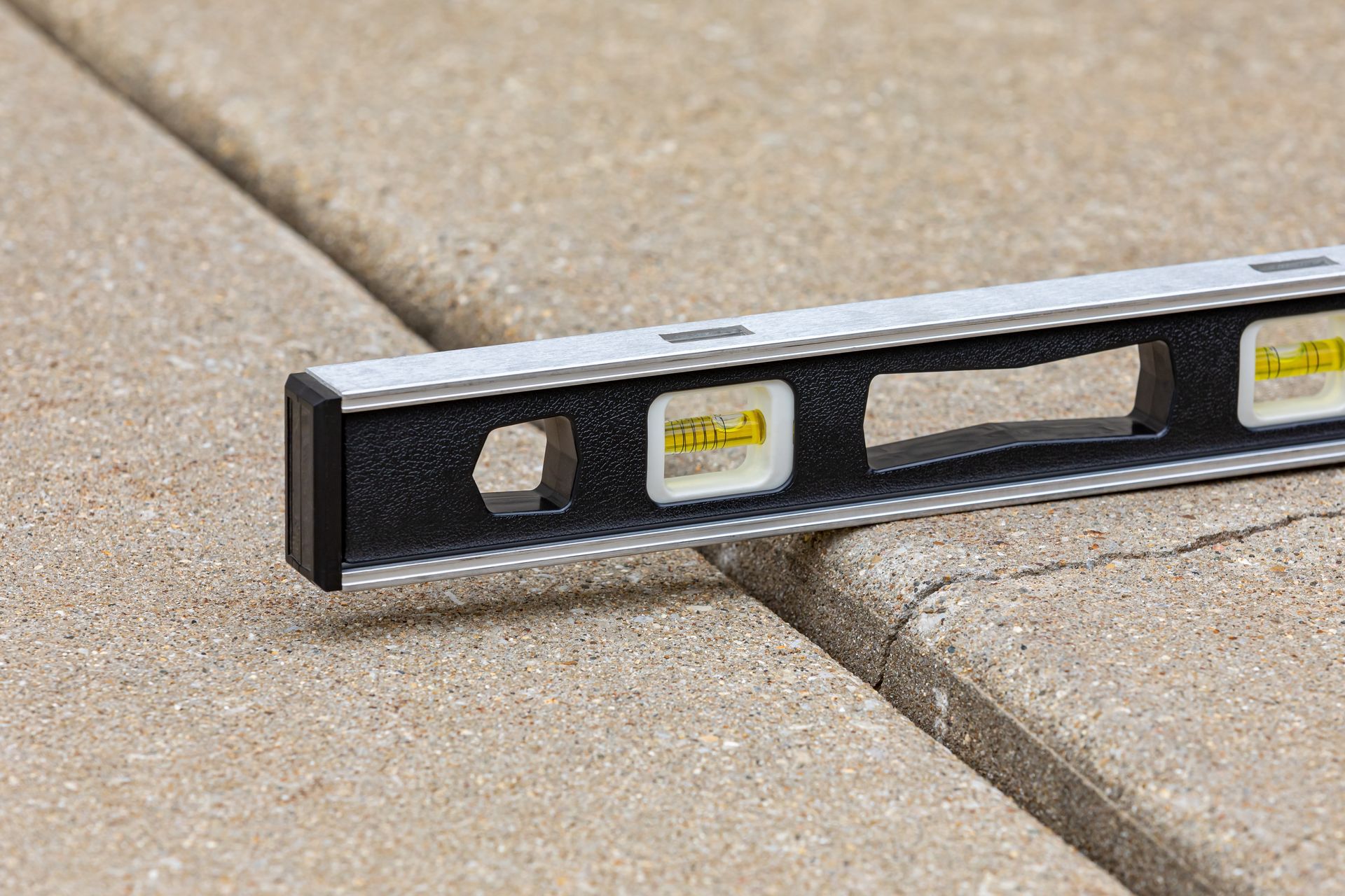 Spirit level on an uneven concrete joint showing a settled slab that needs sunken concrete lifting.