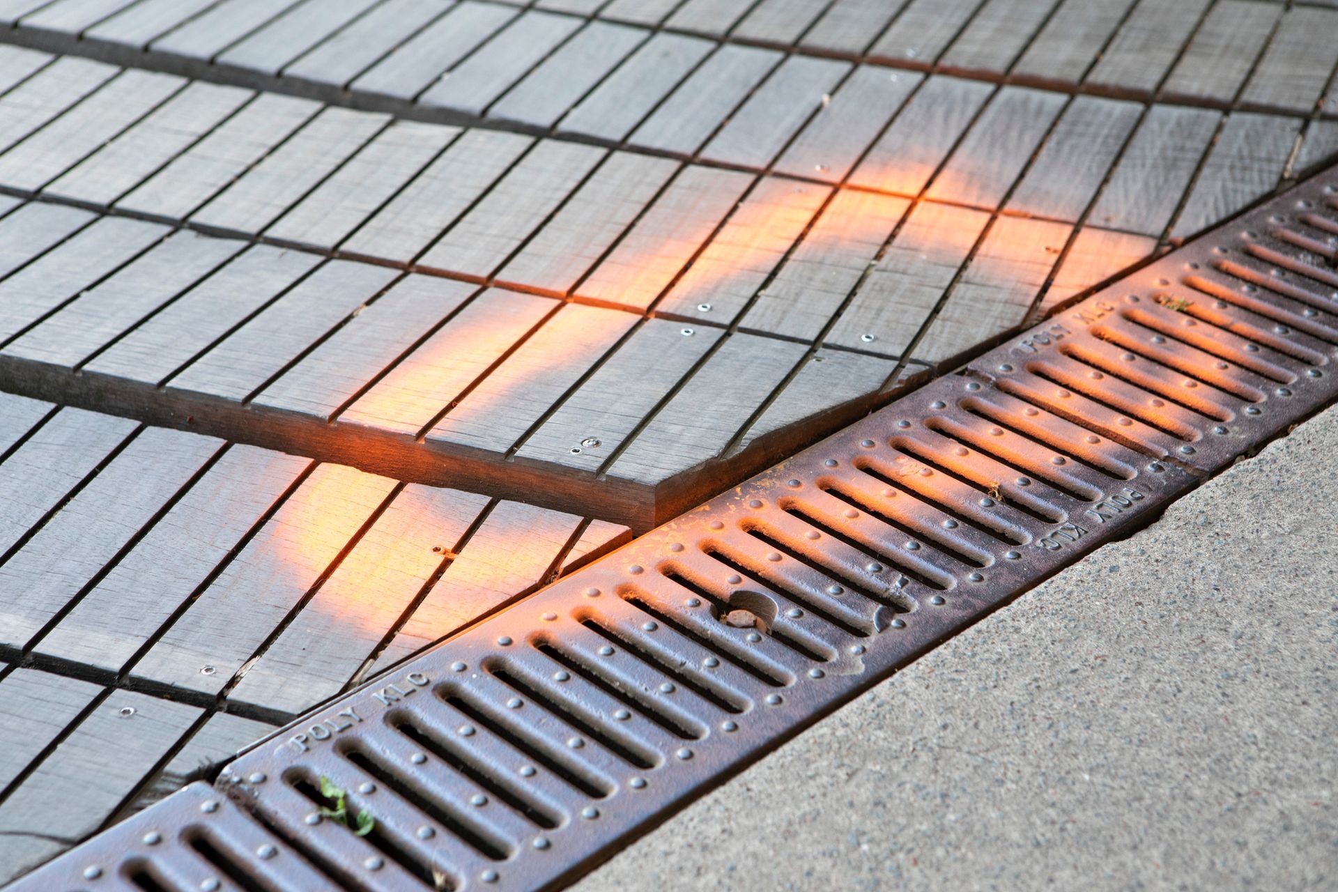 Shadow and sunlight on wooden planks, orange glow near a drain.