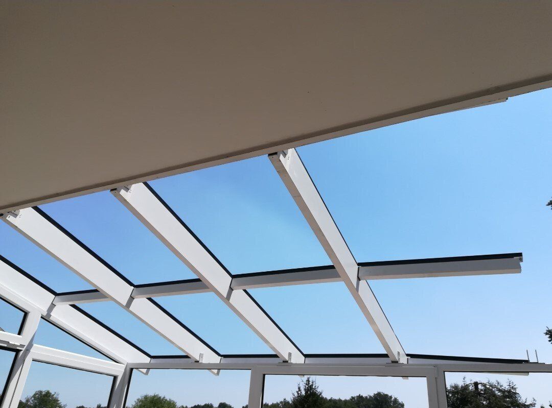 Struttura del tetto in vetro con cornice bianca contro un cielo azzurro terso.