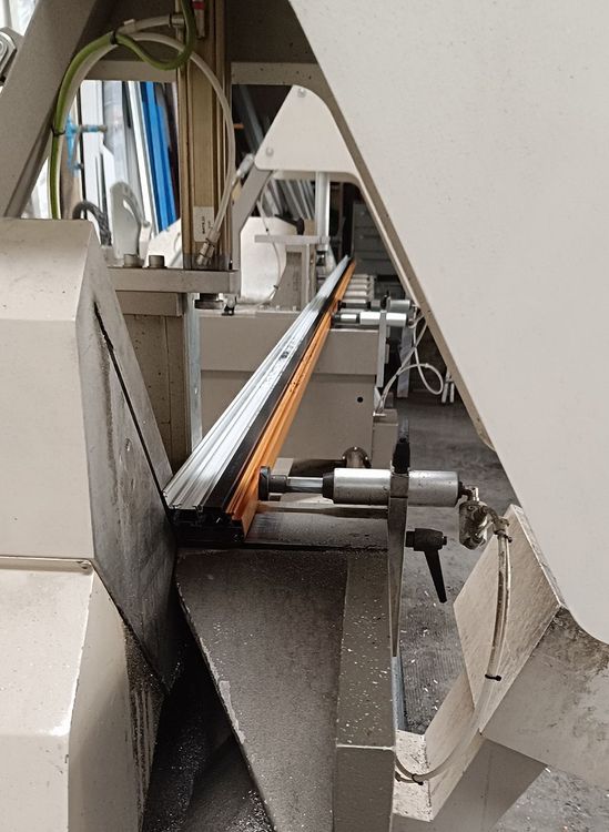 Sega per metalli che taglia una pila di barre metalliche. La macchina è grigia con una lama argentata.
