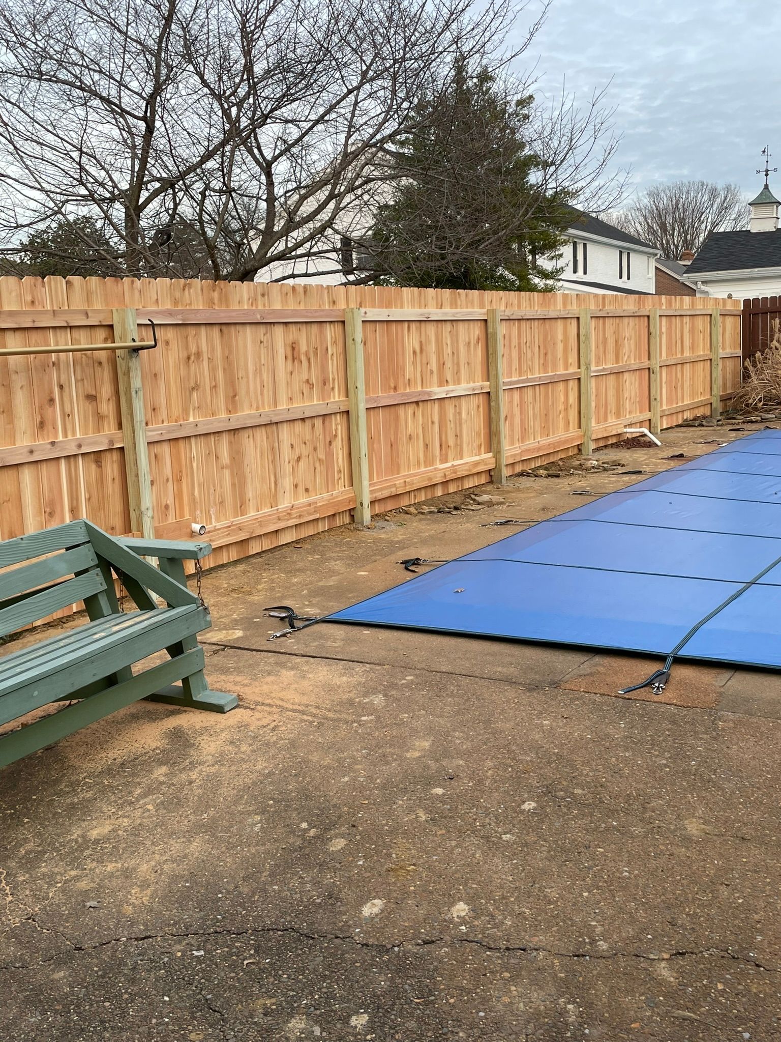 A wooden fence surrounds a swimming pool covered in snow.