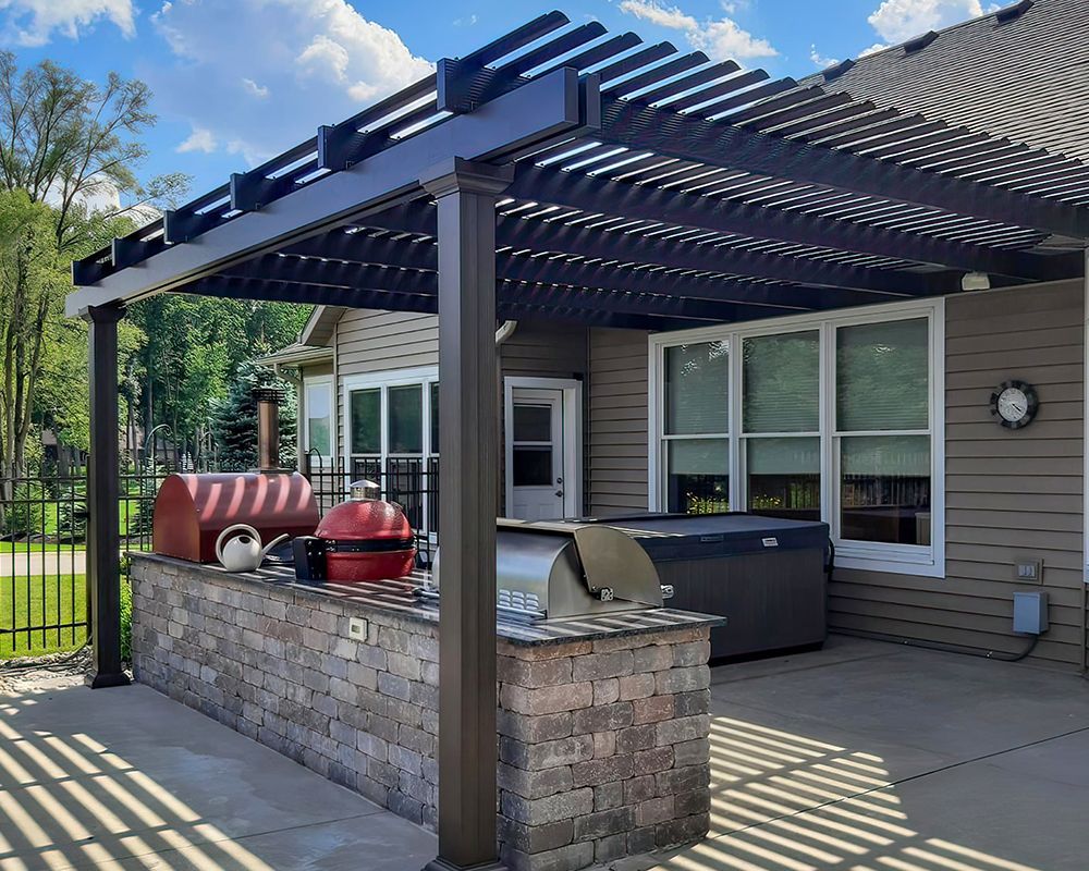 A pergola over a patio with a grill and a hot tub.