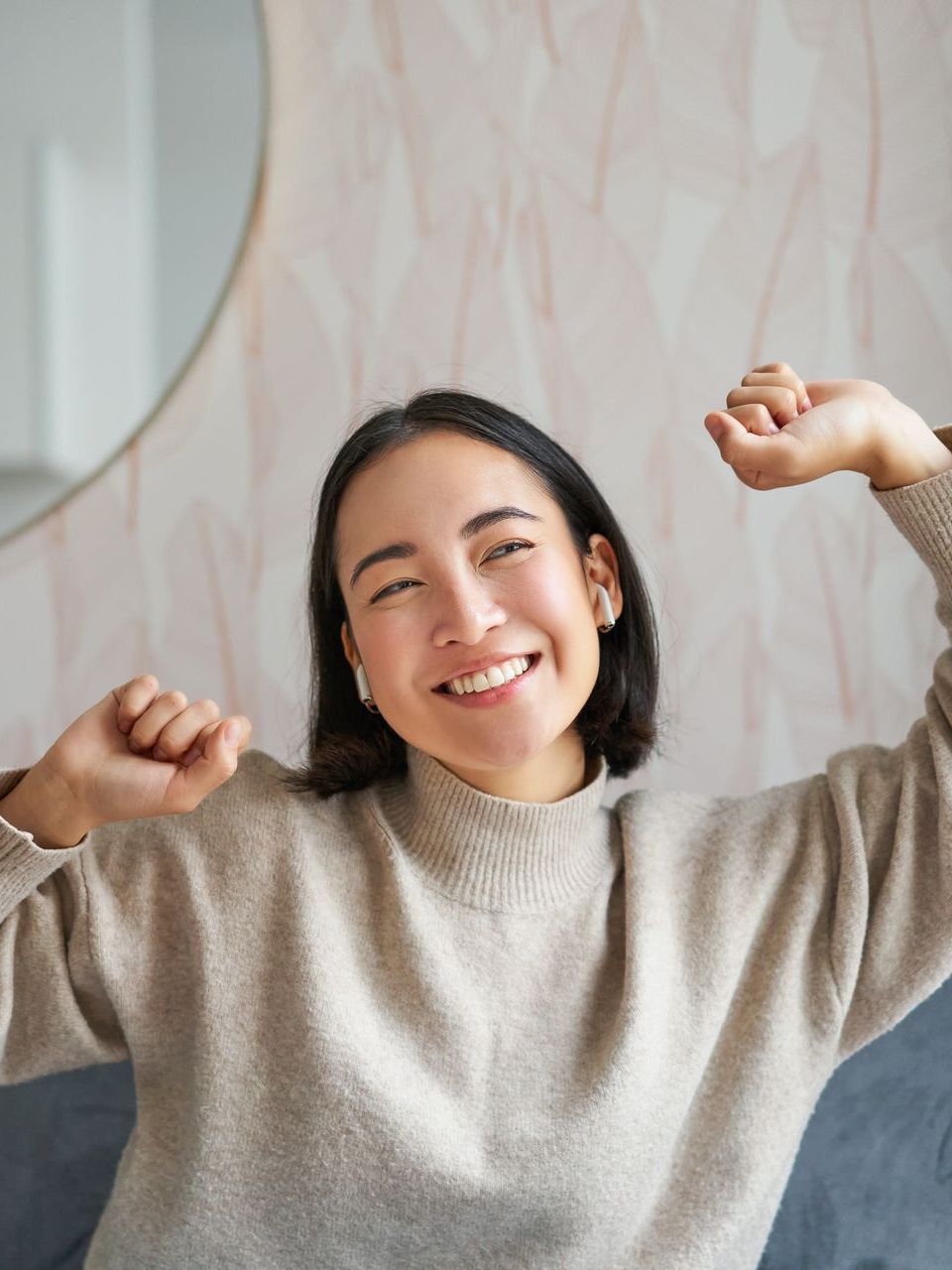 A woman in a sweater is sitting on a couch with her arms in the air.