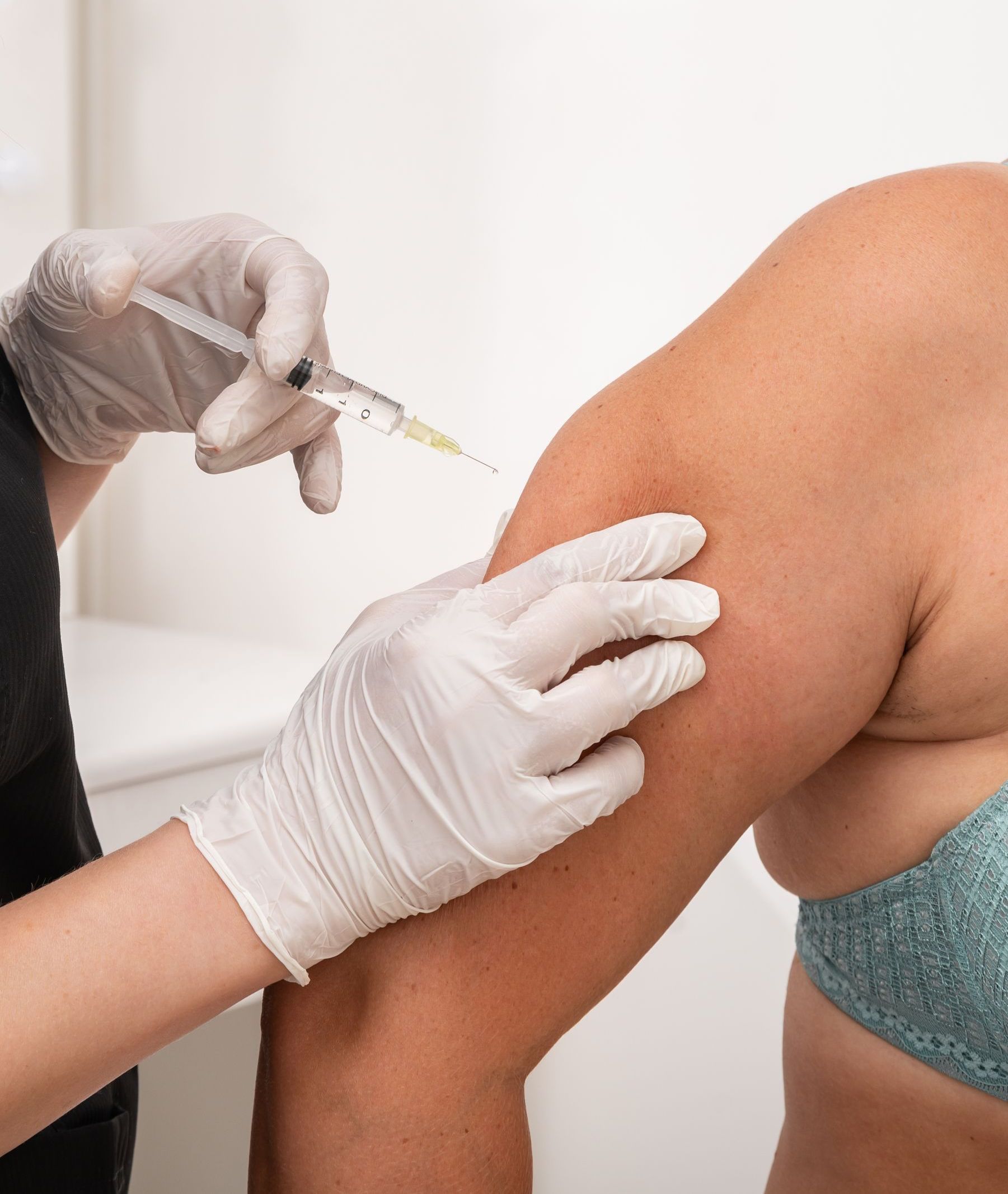 A person receiving an injection in their upper arm. A gloved hand holds a syringe.