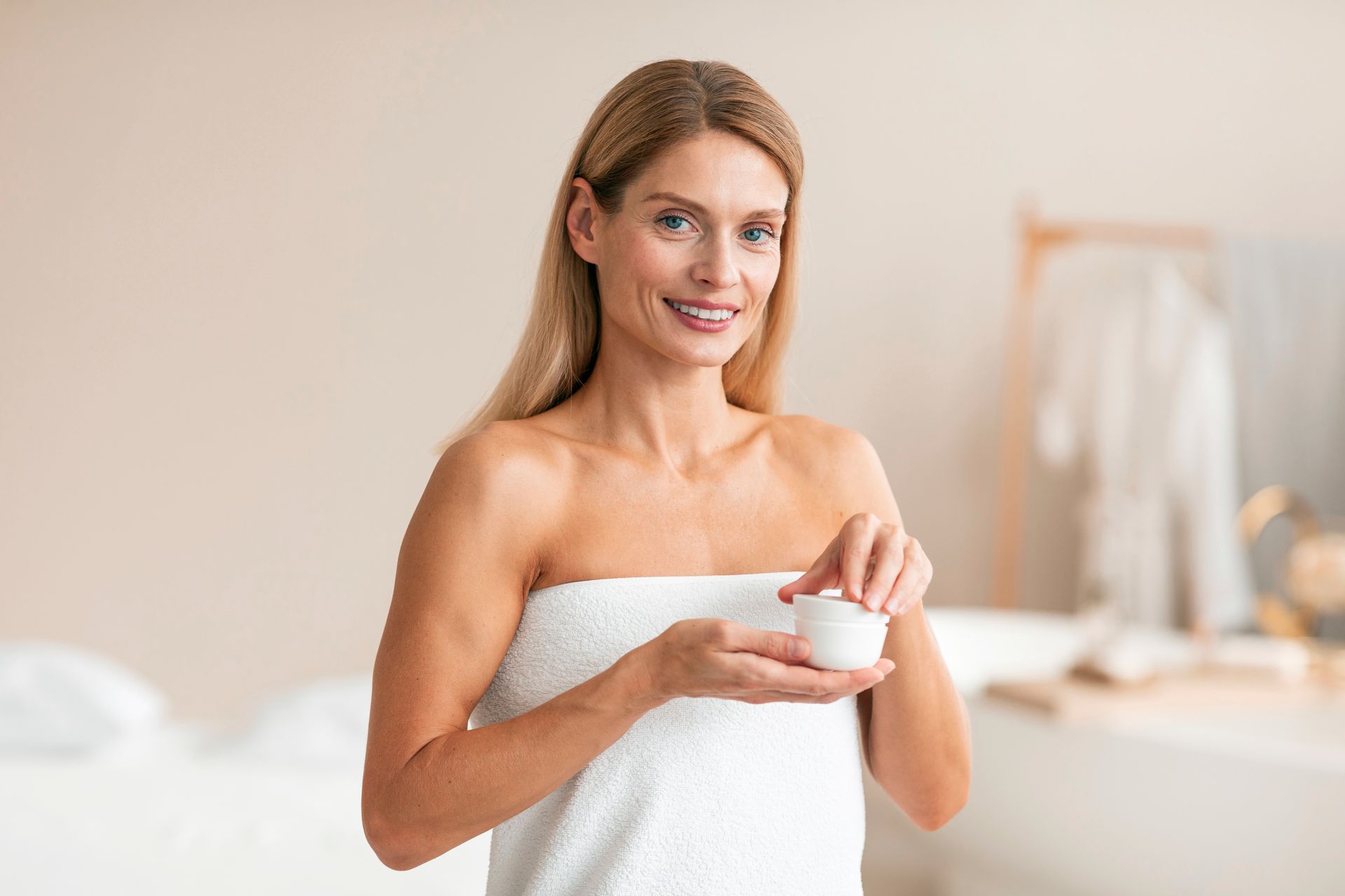 A woman wrapped in a towel is applying cream to her face.